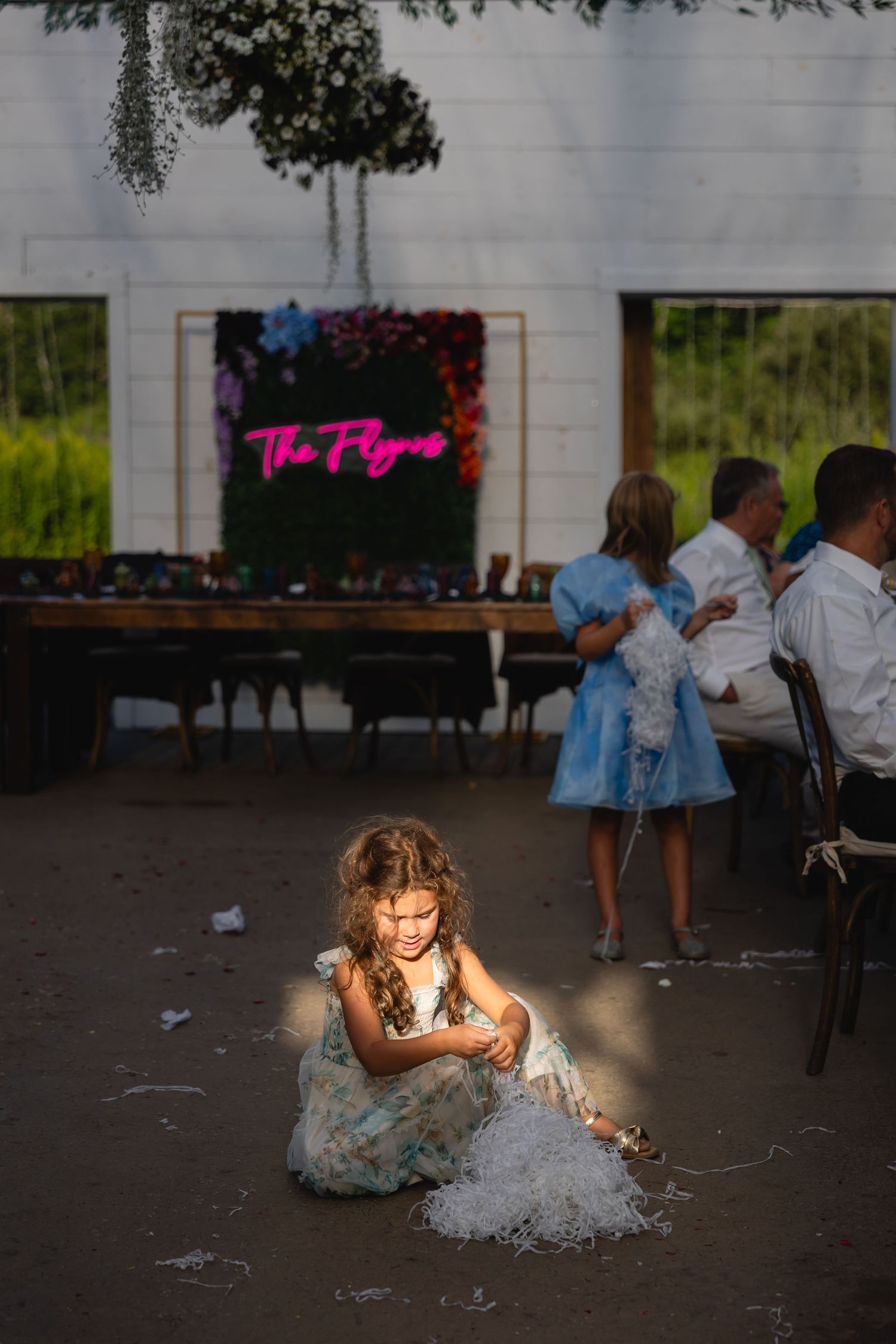 A young guest in a blue dress plays with shimmering confetti on the dance floor at a wedding reception.