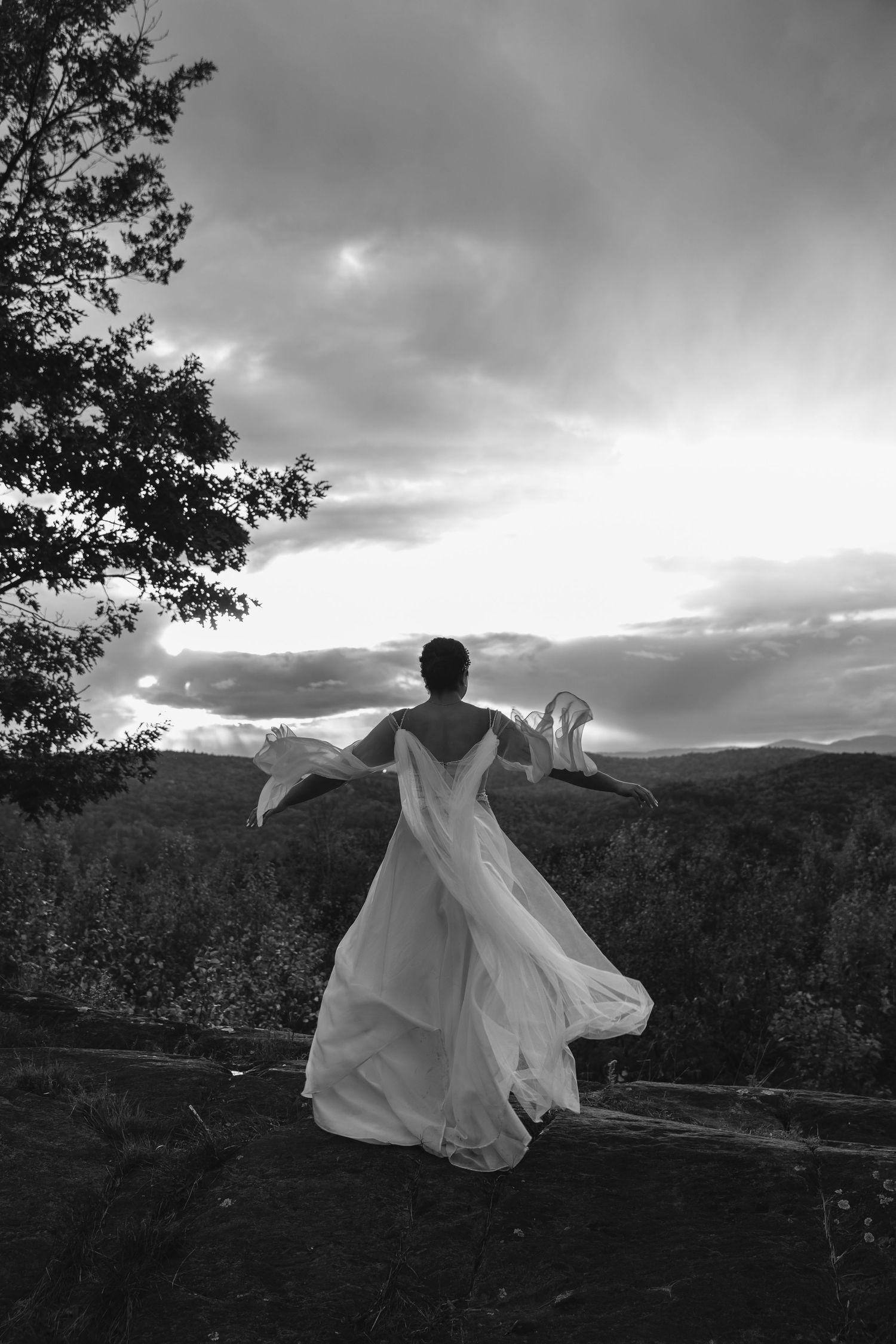 A bride in a flowing white dress twirls against a dramatic mountain sunset backdrop.