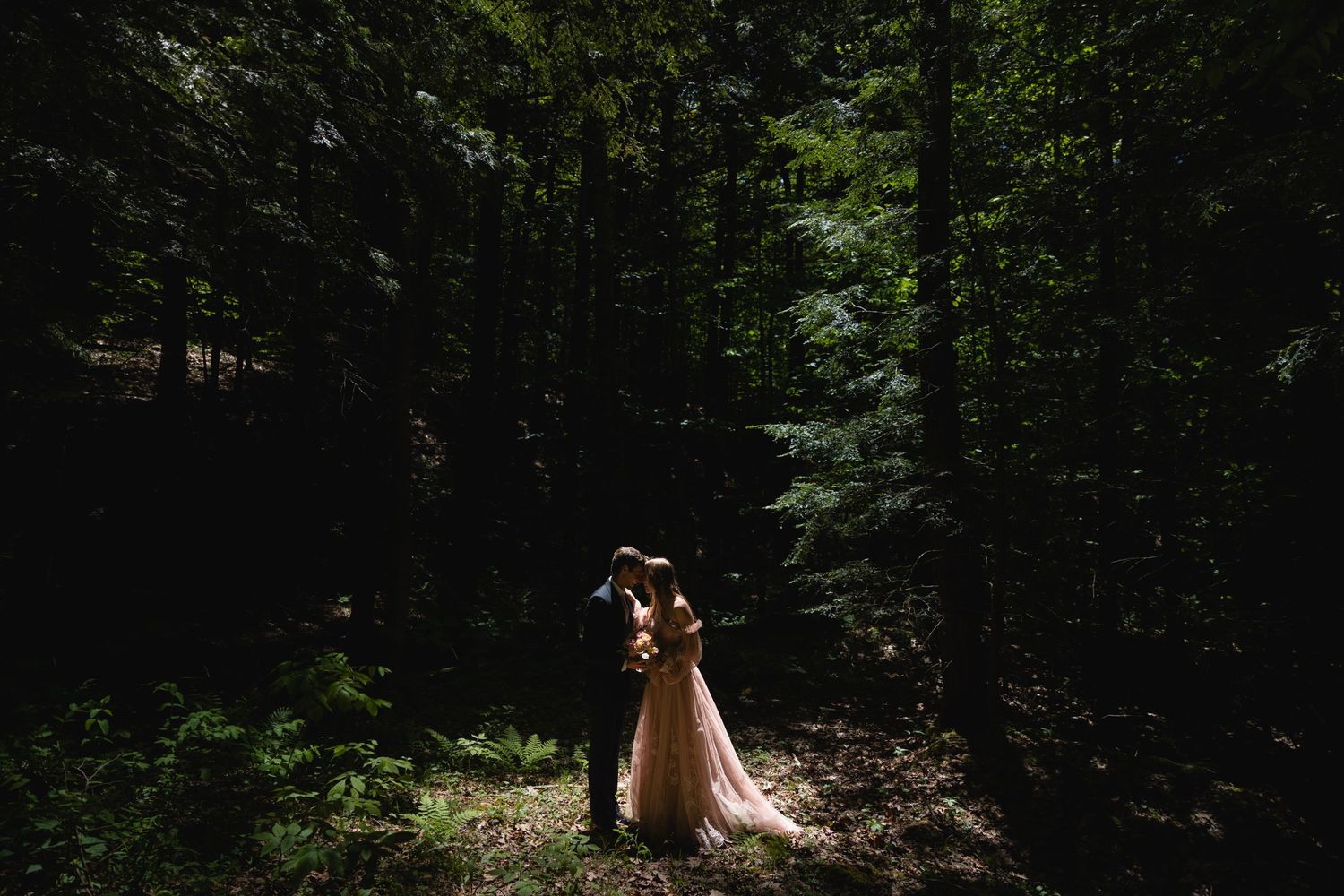 A romantic woodland wedding portrait with sunlight streaming through the trees.