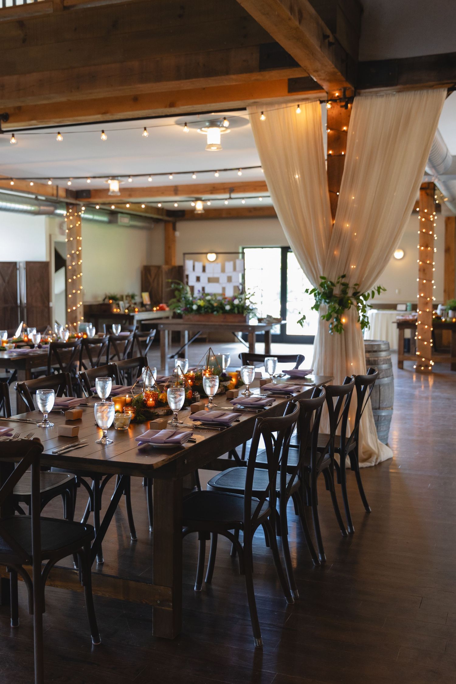 Elegant wedding reception venue with draped fabric, string lights, and farm tables set for dinner.