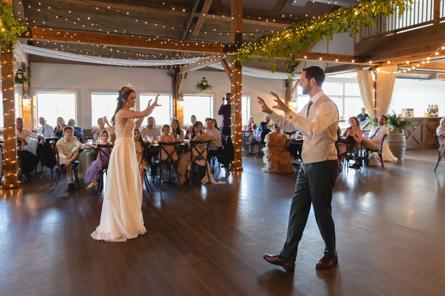 Dancing couple in a rustic venue decorated with string lights and greenery.