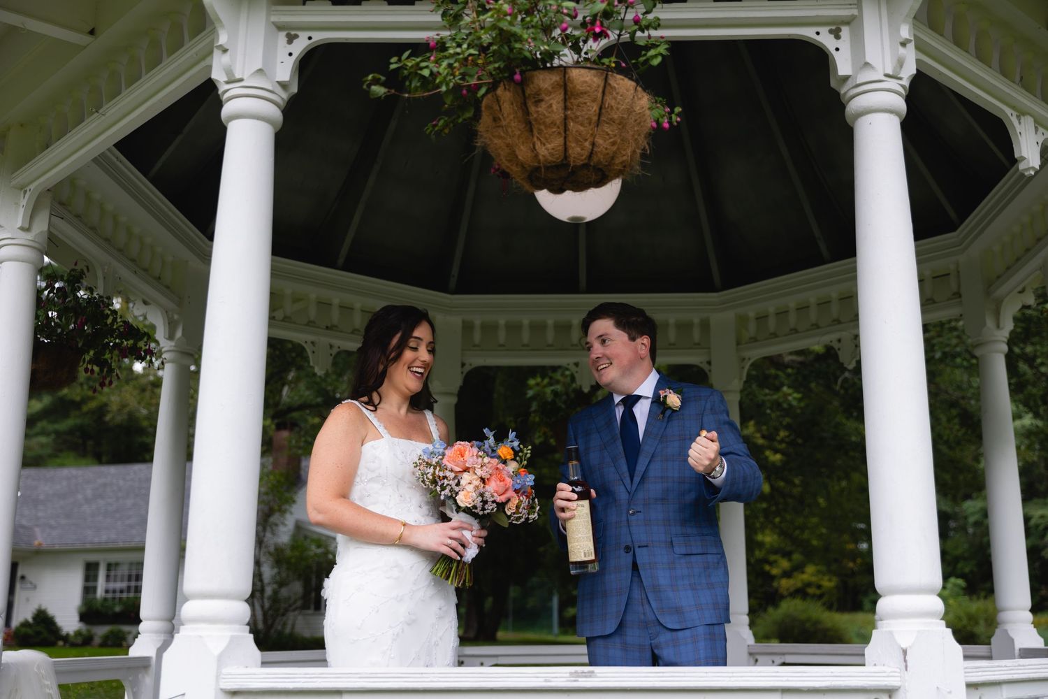 A couple shares a joyful moment under an ornate white gazebo during their wedding ceremony.