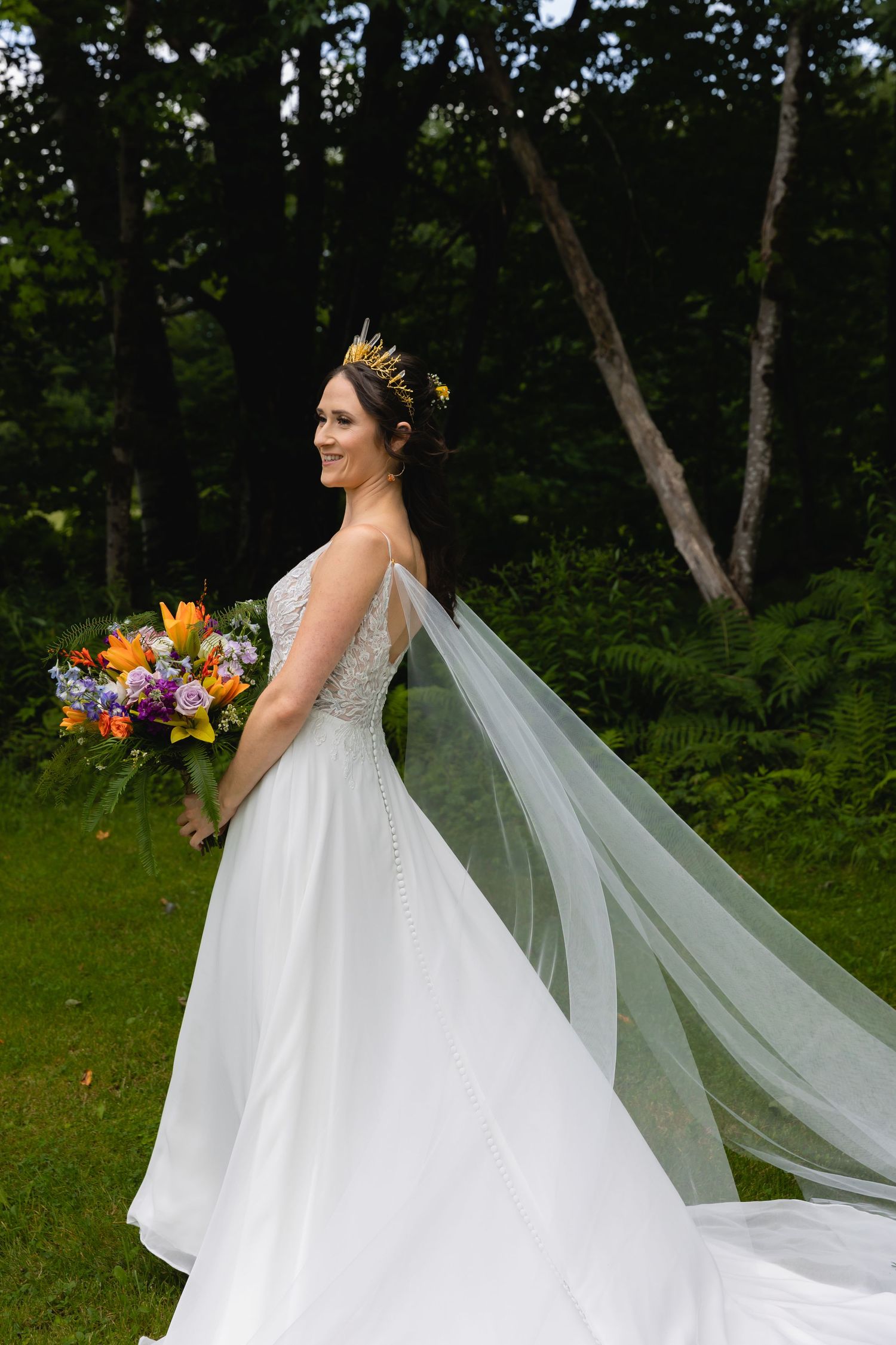 A wedding dress with long veil and colorful bouquet photographed against a woodland backdrop.
