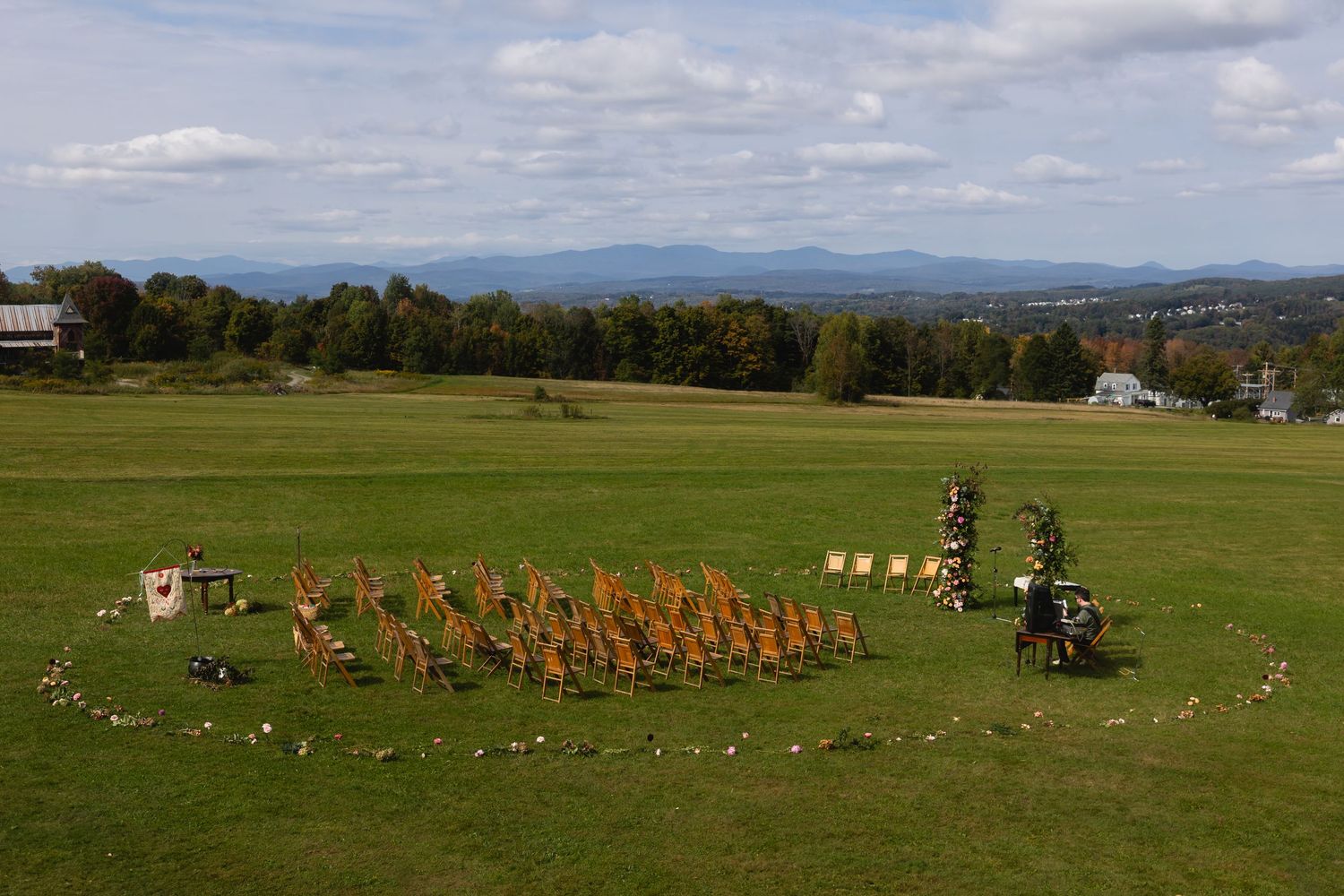 Aerial view of orange pumpkins arranged in a spiral pattern on green grass field with mountains in the background.
