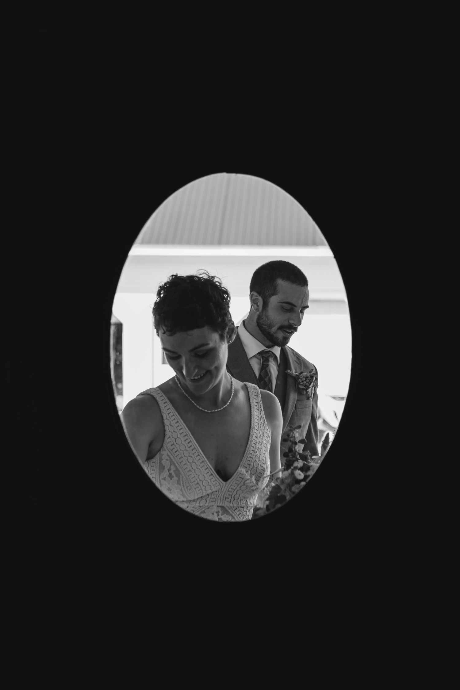 Black and white oval-framed portrait of a smiling bride and groom at their wedding.