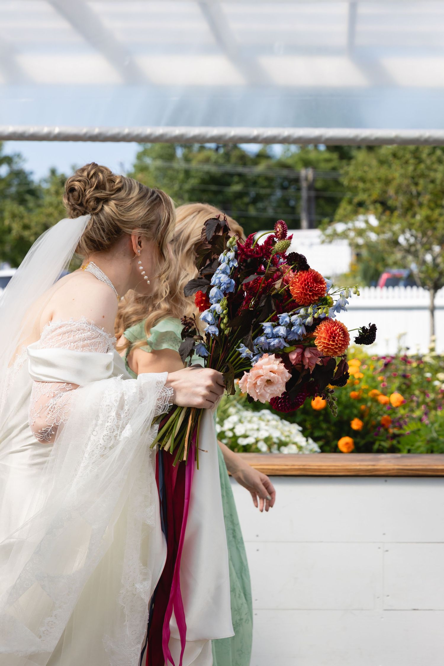 Wedding bouquet with deep burgundy ribbons and colorful flowers against a bright outdoor background.
