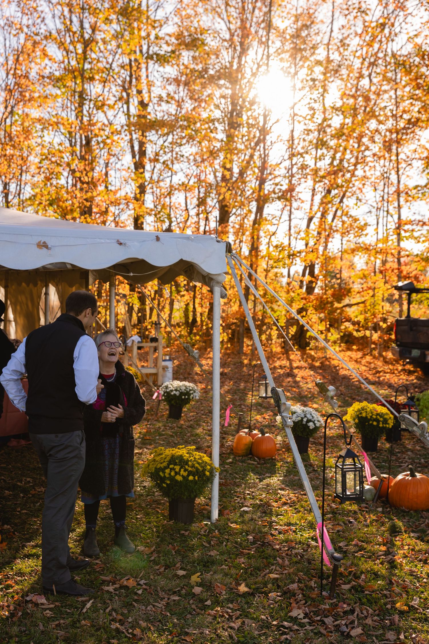 An outdoor autumn wedding ceremony setup with white tent and pumpkin decorations among golden fall foliage.