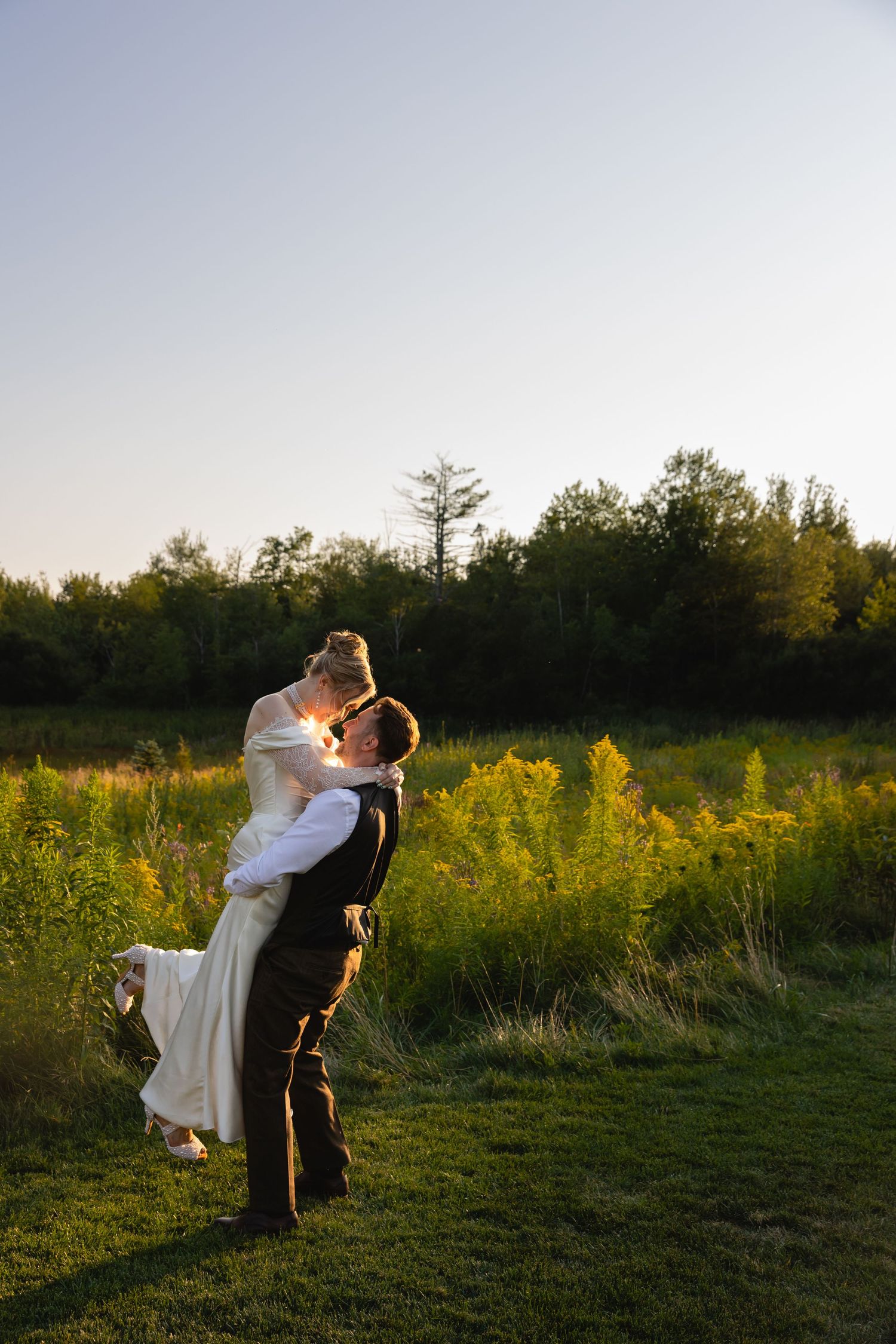 A couple shares a romantic dip pose in a golden wildflower field at sunset.