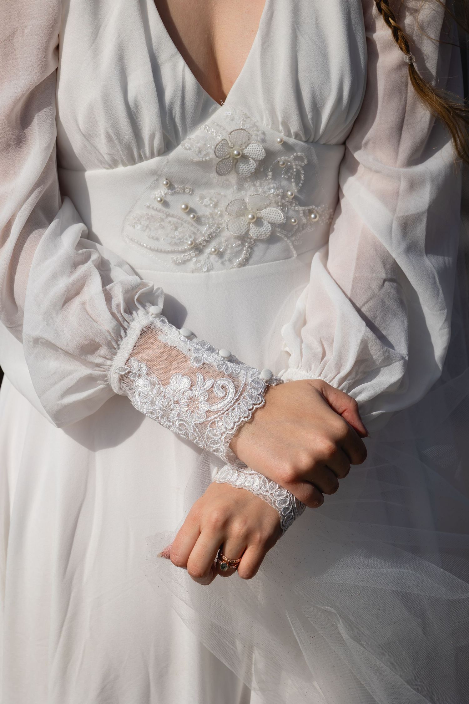 Close-up details of a white wedding dress with delicate lace trim and sheer long sleeves.