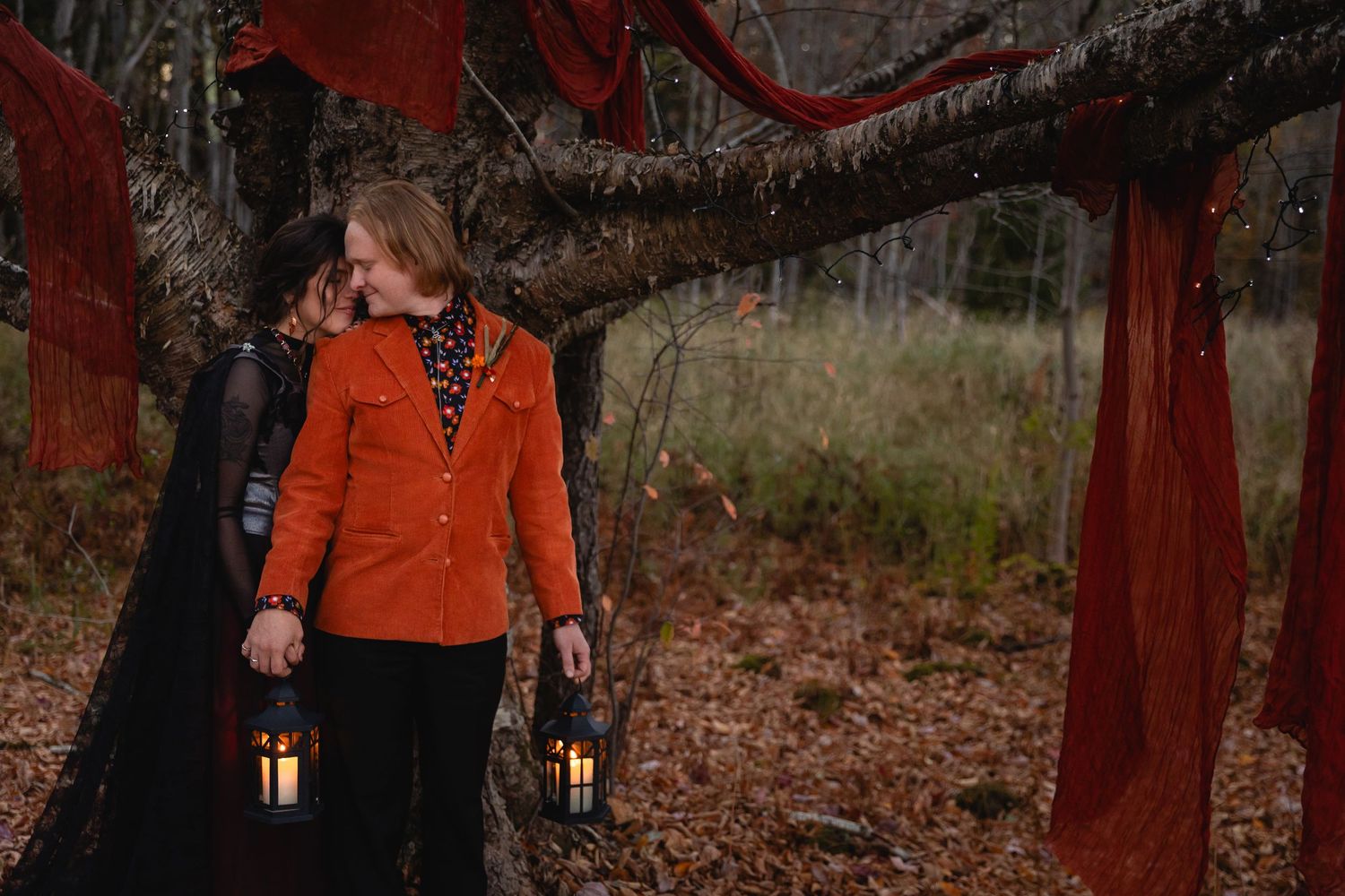 A group of people in orange jackets walk through a dark forest carrying lanterns during a nighttime tour.