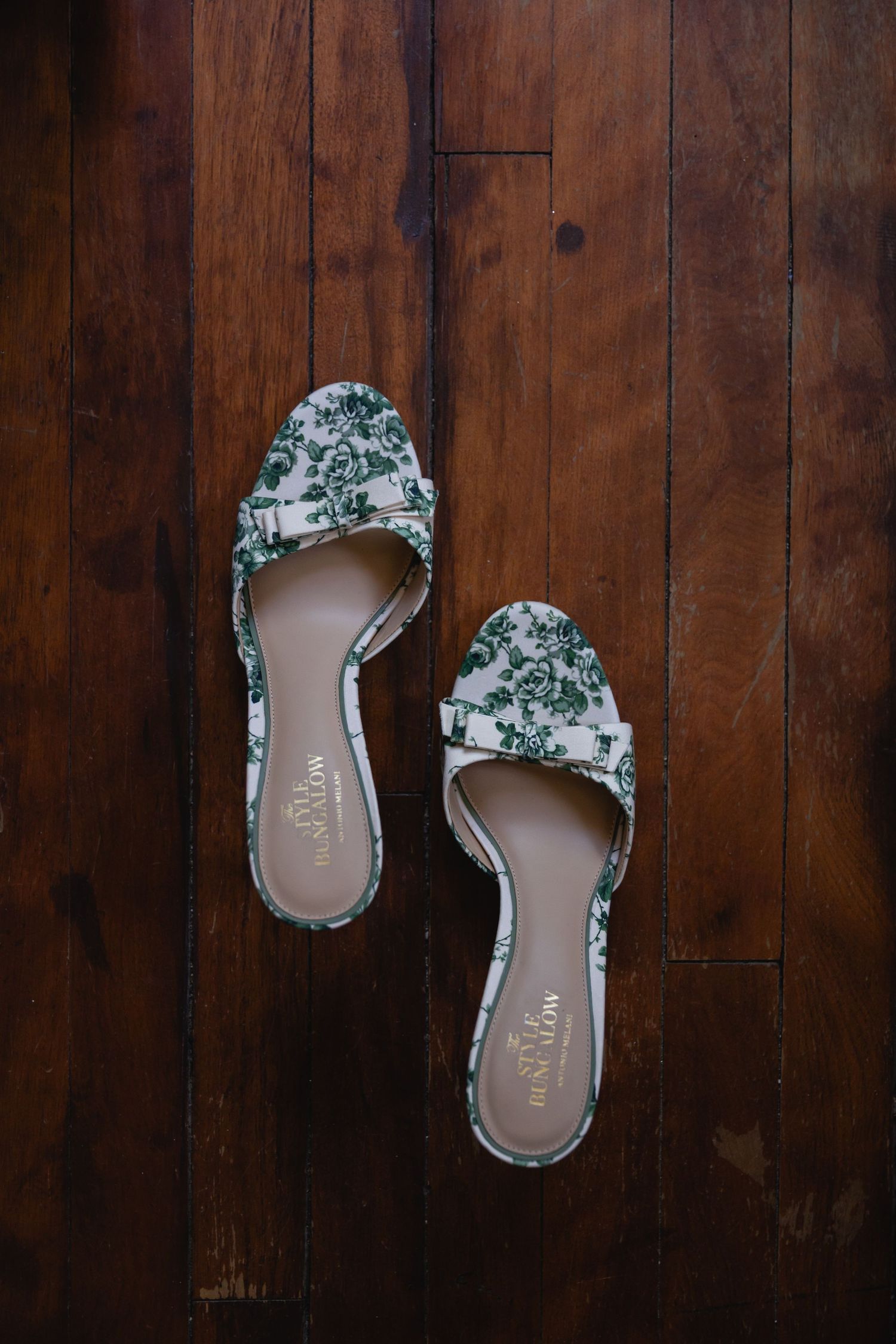 Floral patterned wedding shoes arranged on a rustic wooden floor.