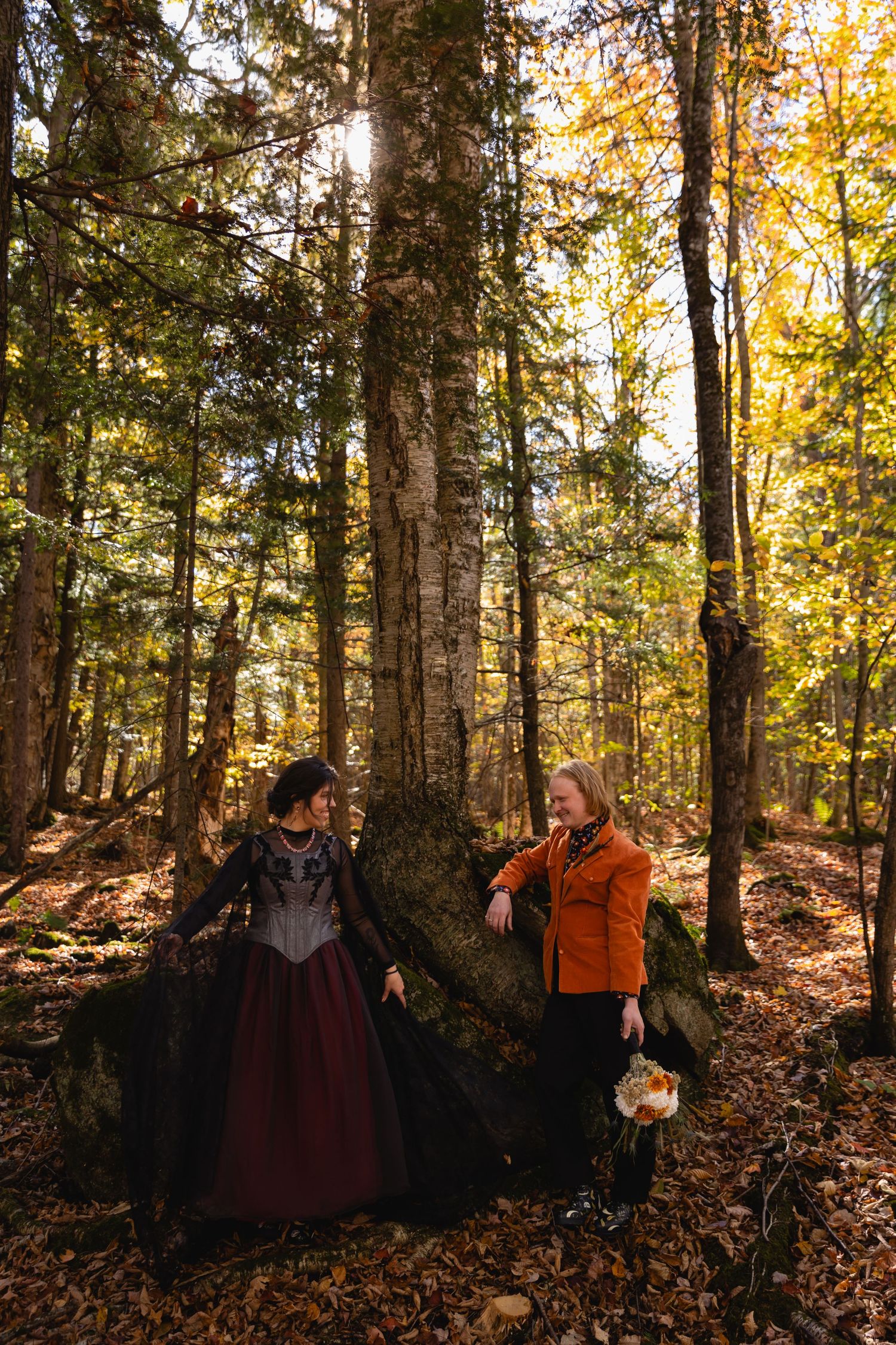 A group stands together in a sunlit autumn forest with golden leaves and tall trees during a fall photoshoot.