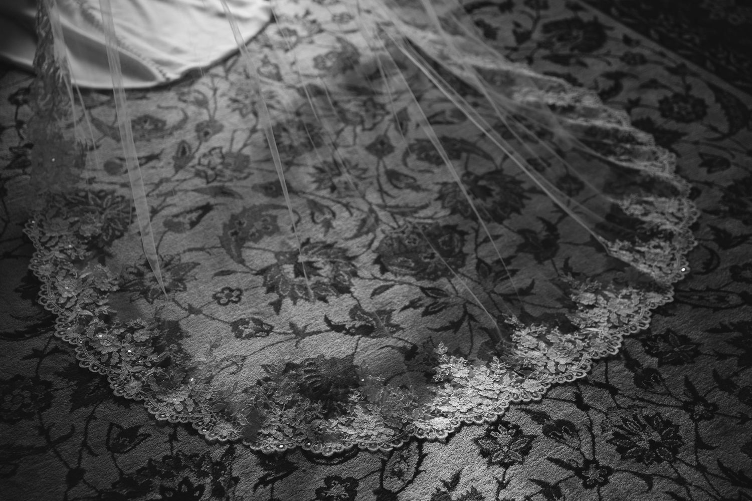 A black and white close-up photograph shows intricate lace fabric with delicate floral patterns and textural details.