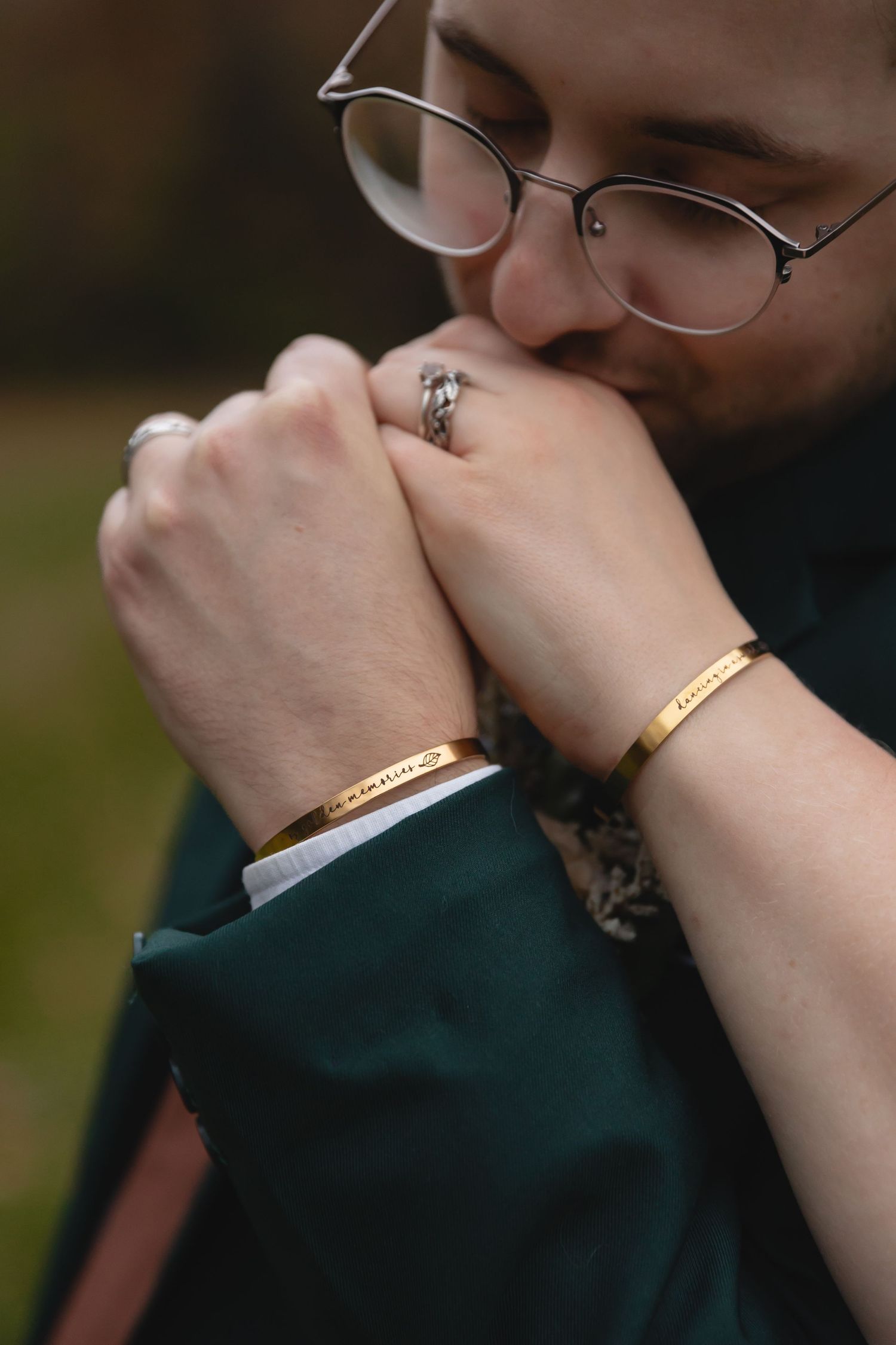 Close up of matching gold bracelets and engagement ring being kissed.