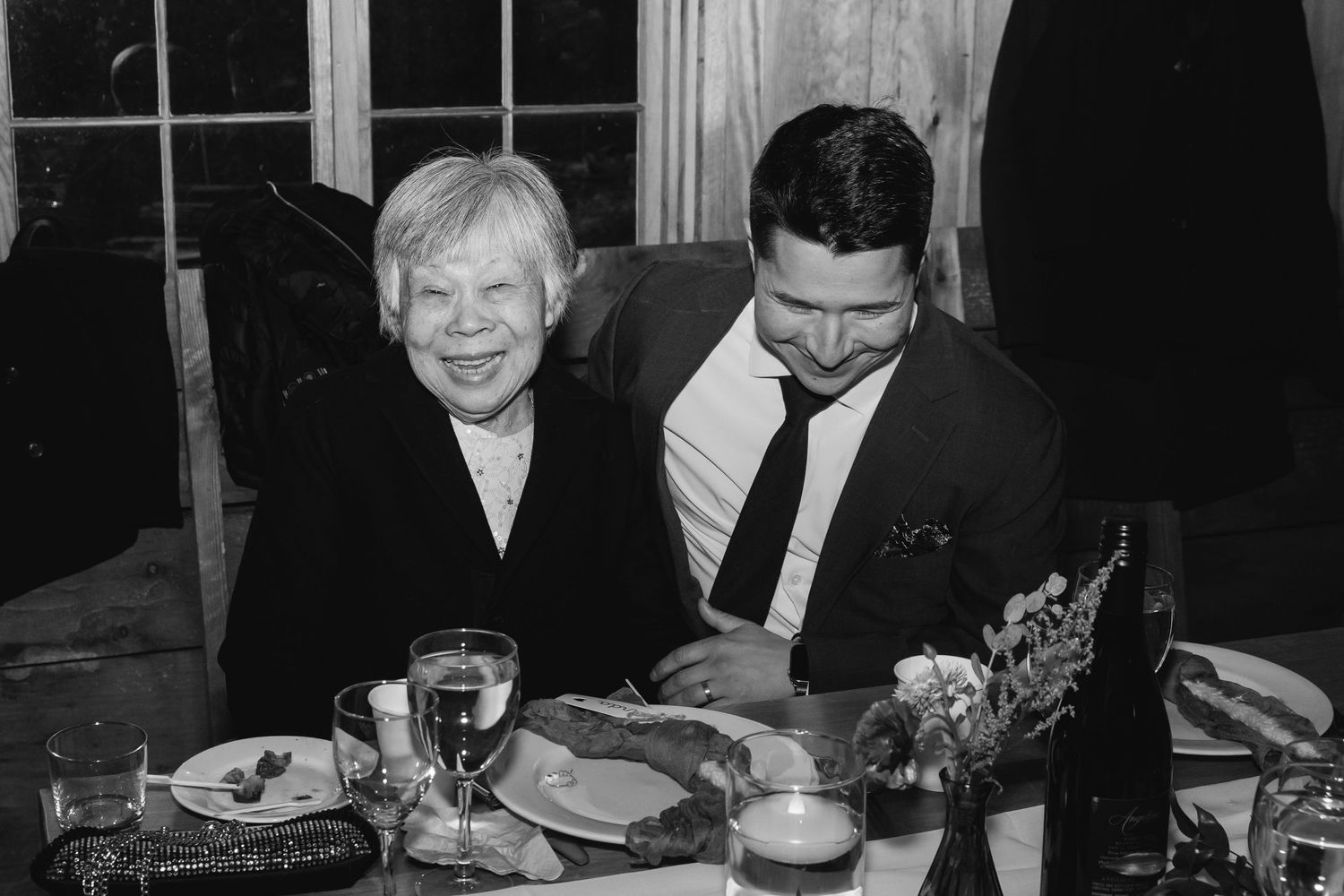 Two people sitting at a dinner table sharing a moment together in black and white photography.