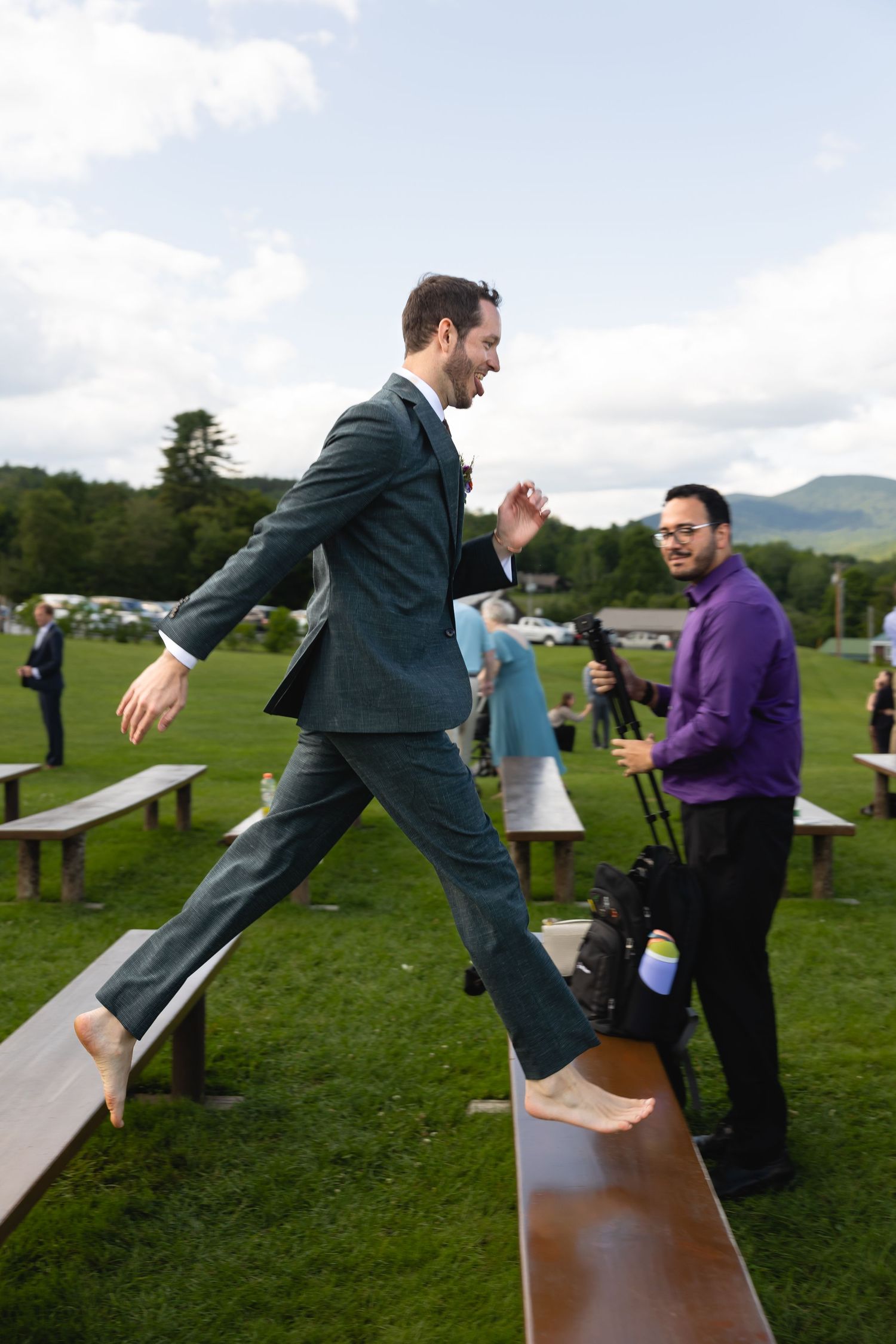 Someone walking across a wooden bench at an outdoor gathering with mountains in the background.