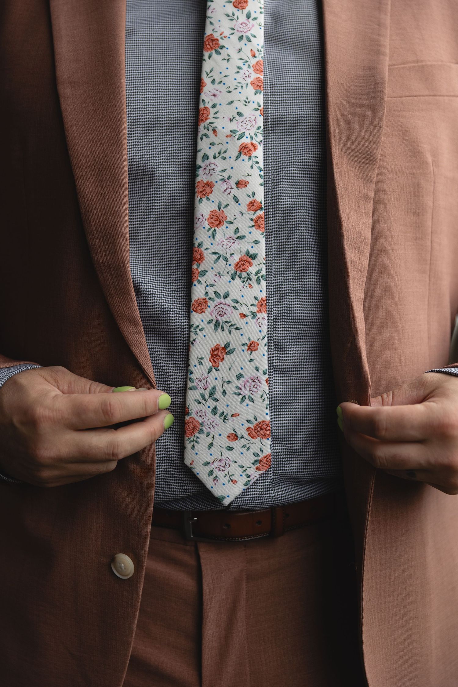 Close-up of a stylish floral tie against a grey shirt and brown suit jacket.