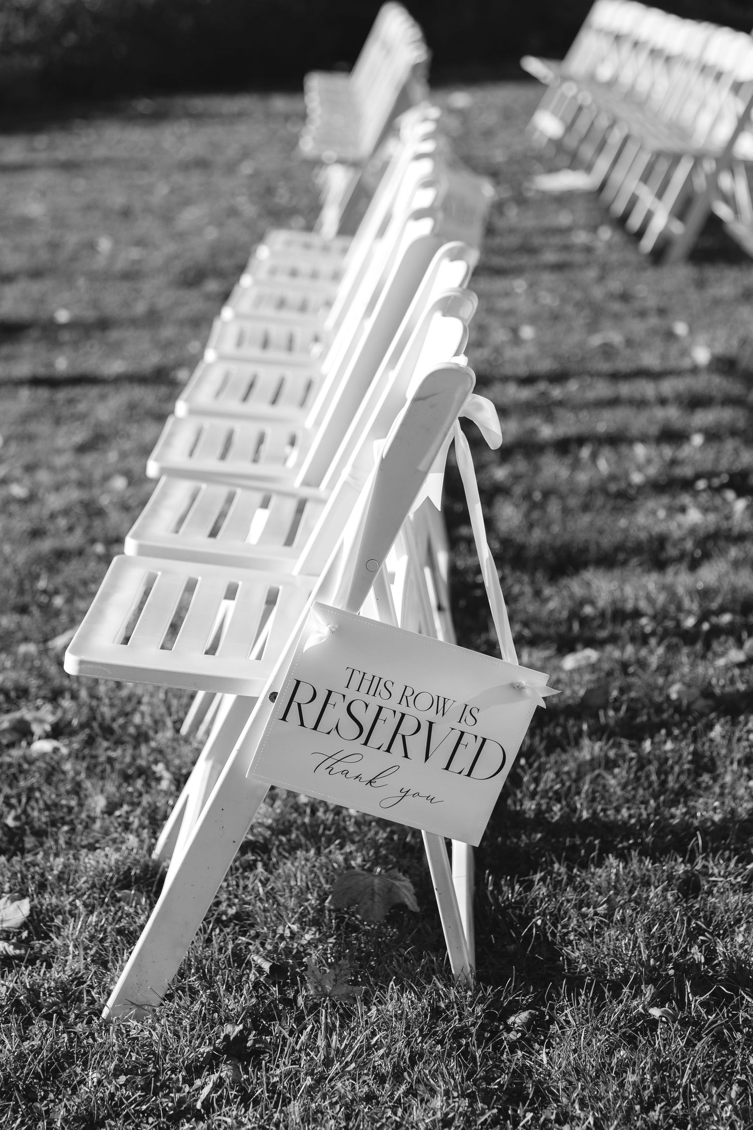 Row of white wooden folding chairs with reserved signs set up for an outdoor wedding ceremony.