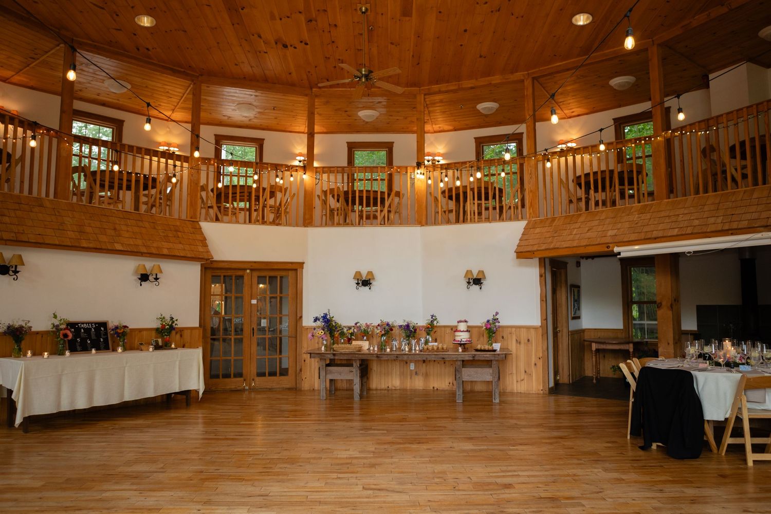 Rustic wooden event venue with balcony and white-clothed tables.