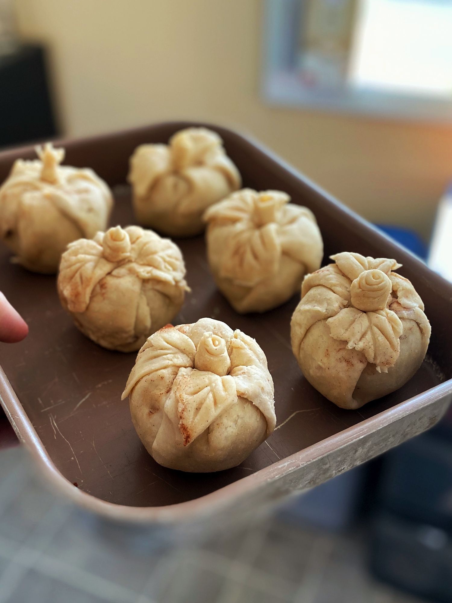 Six golden-baked decorative dumpling buns with flower-shaped tops arranged on a brown baking tray.