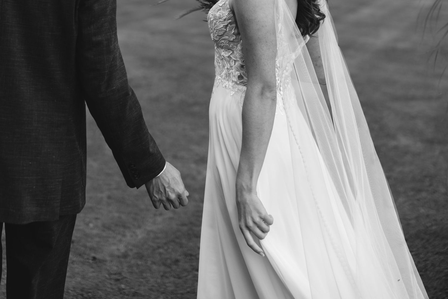 Close-up of wedding dress details and couple holding hands in black and white.