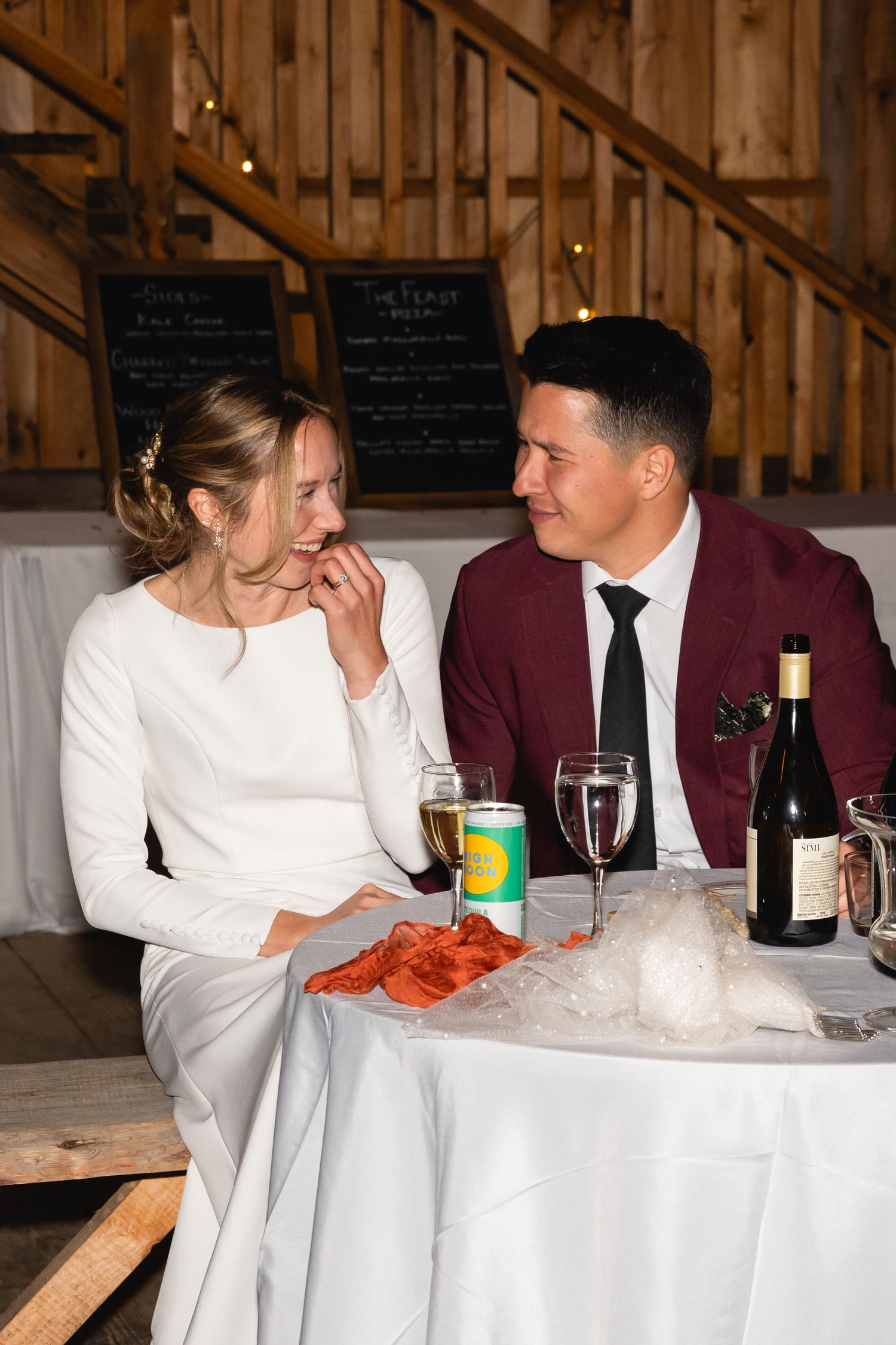 Wedding couple enjoying lobster dinner together at rustic venue with wine and beverages on white tablecloth.