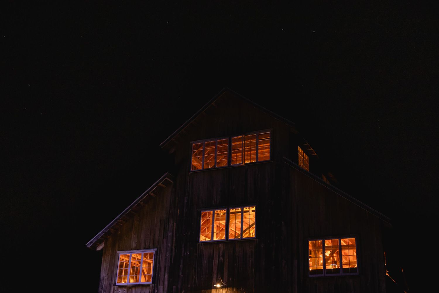 A dark barn illuminated from within by warm orange lights glowing through its windows at night.