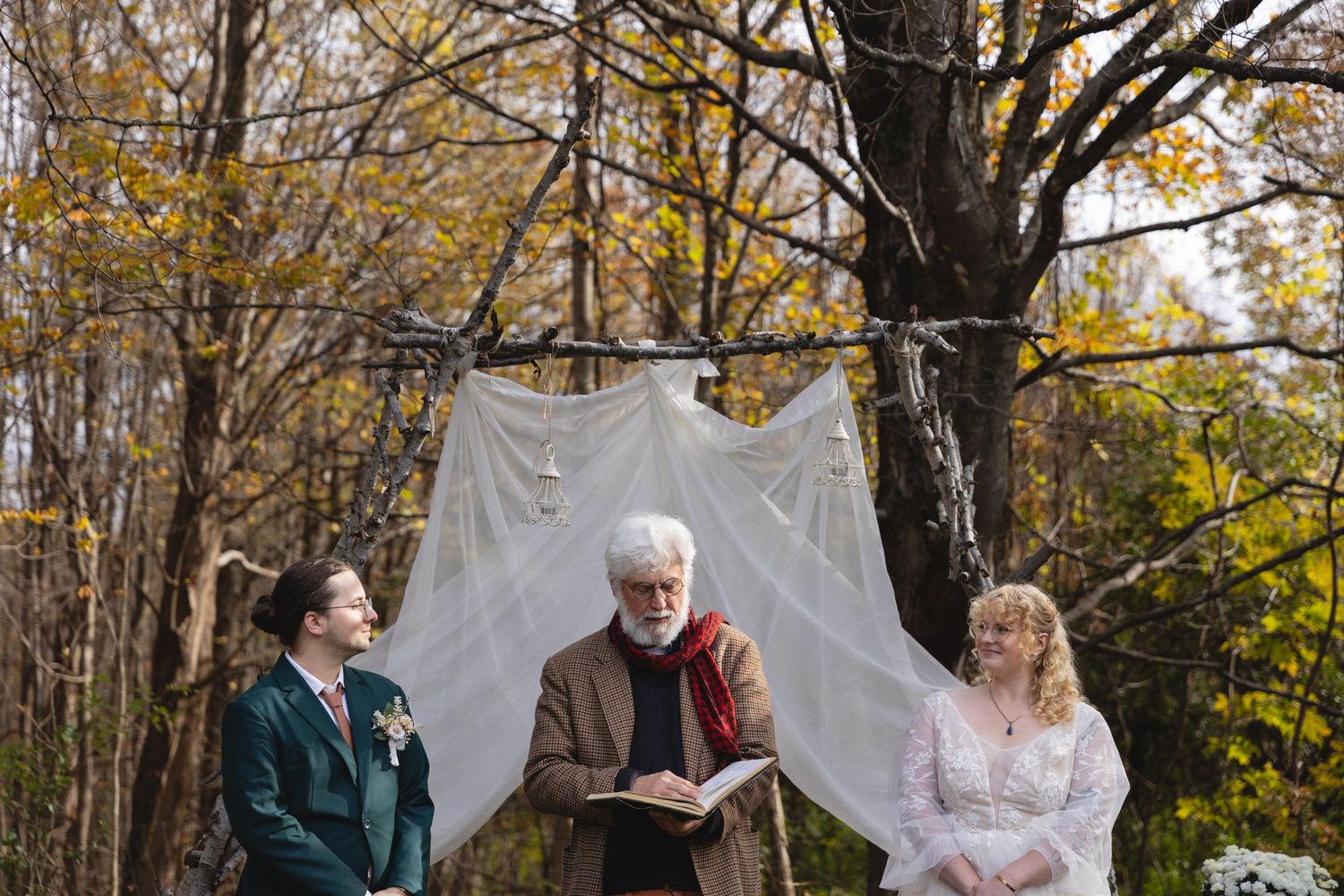 Outdoor wedding ceremony with white backdrop amid fall foliage.
