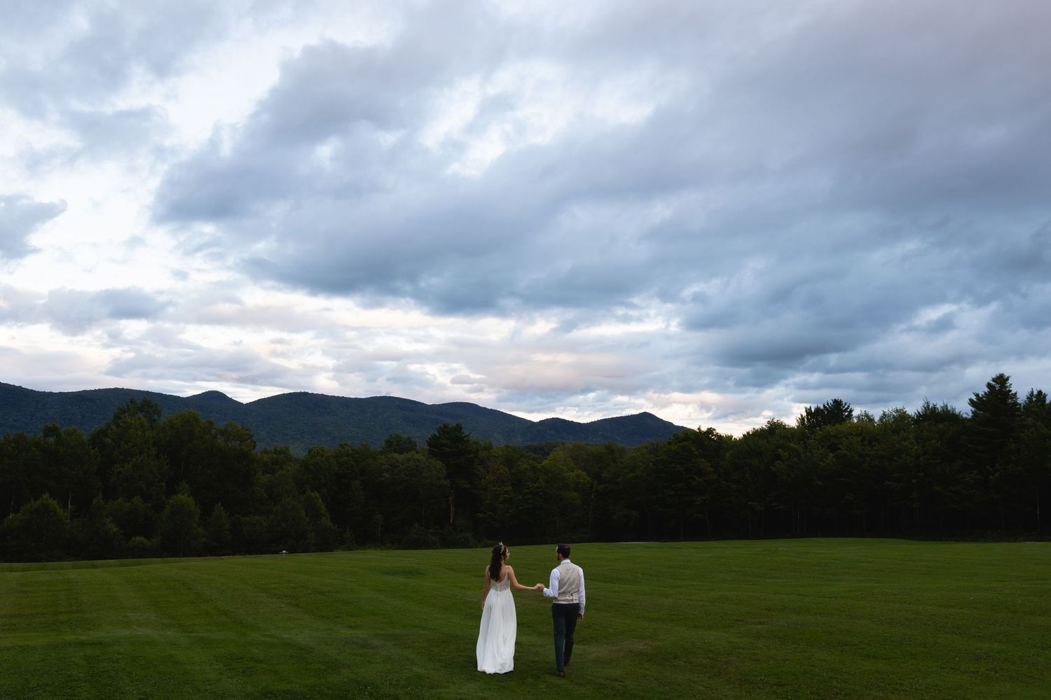 Distant silhouette of couple walking on grass field with mountain backdrop.