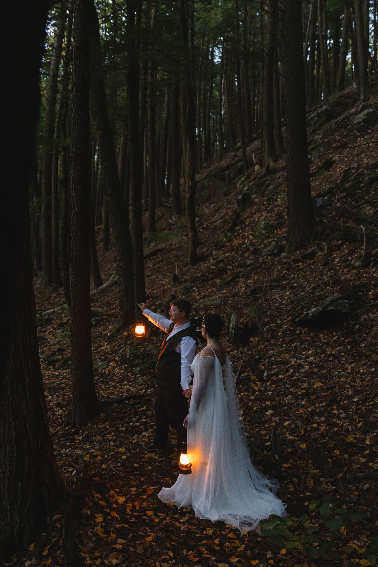 A romantic evening wedding photo with glowing lanterns in a dark forest setting.