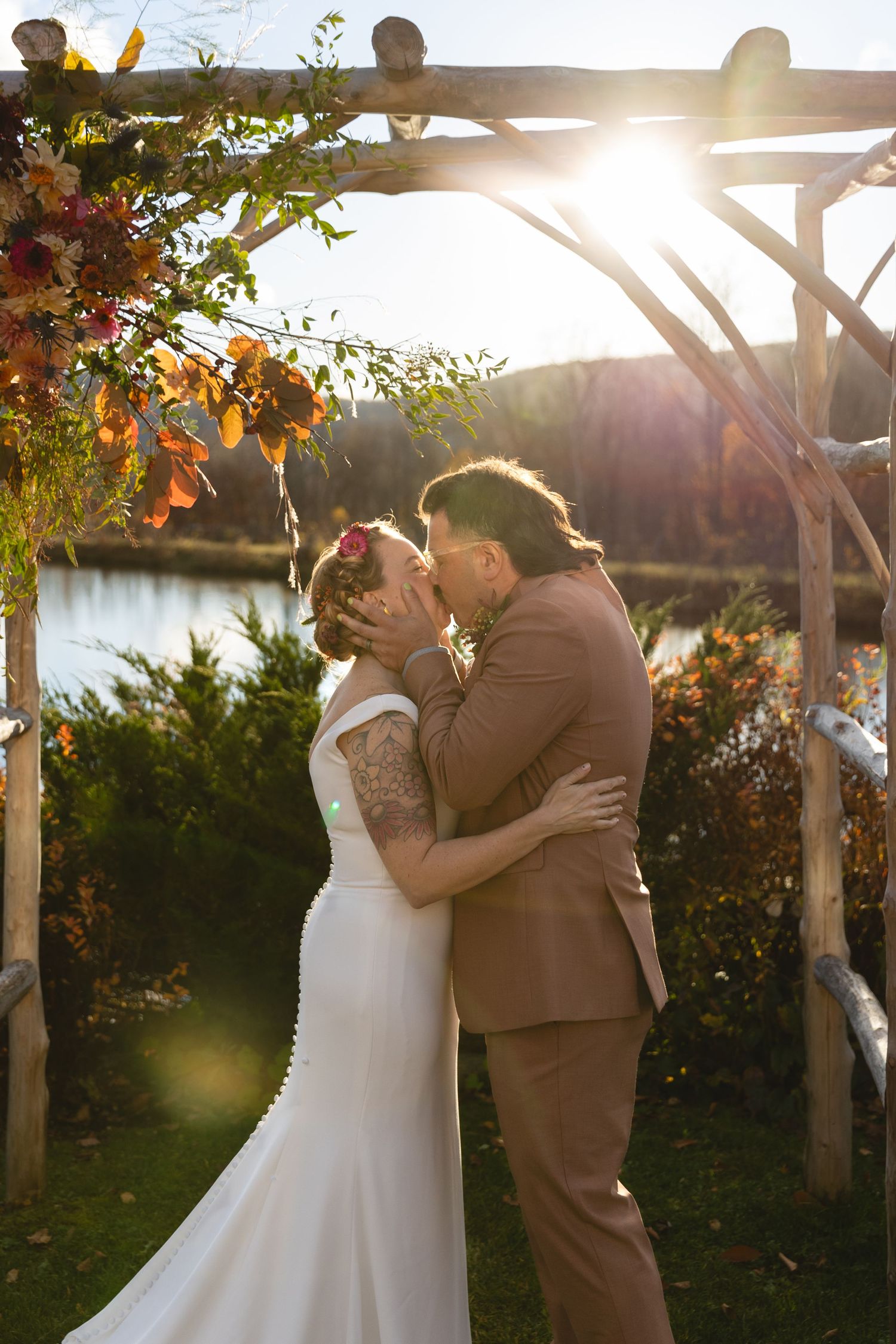 Newlyweds share an intimate moment under a rustic arch with sunset light streaming through.