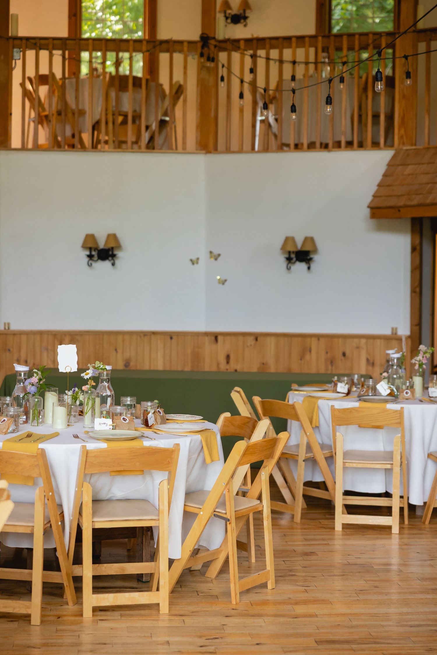 Rustic wooden reception hall with elegant white tablecloths and natural lighting streaming through windows.