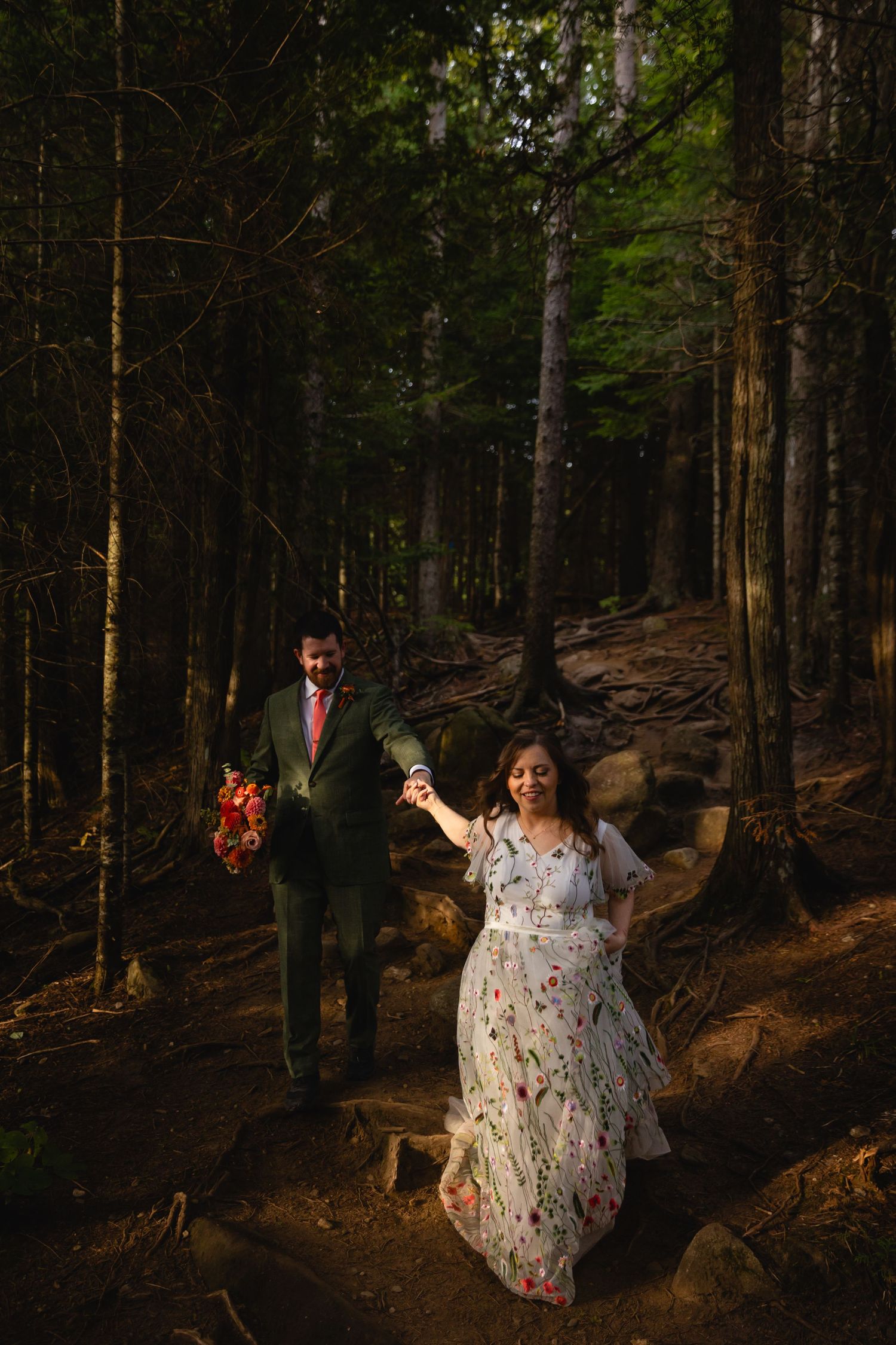 A person in a floral dress twirls joyfully through a sunlit forest path among tall pine trees.