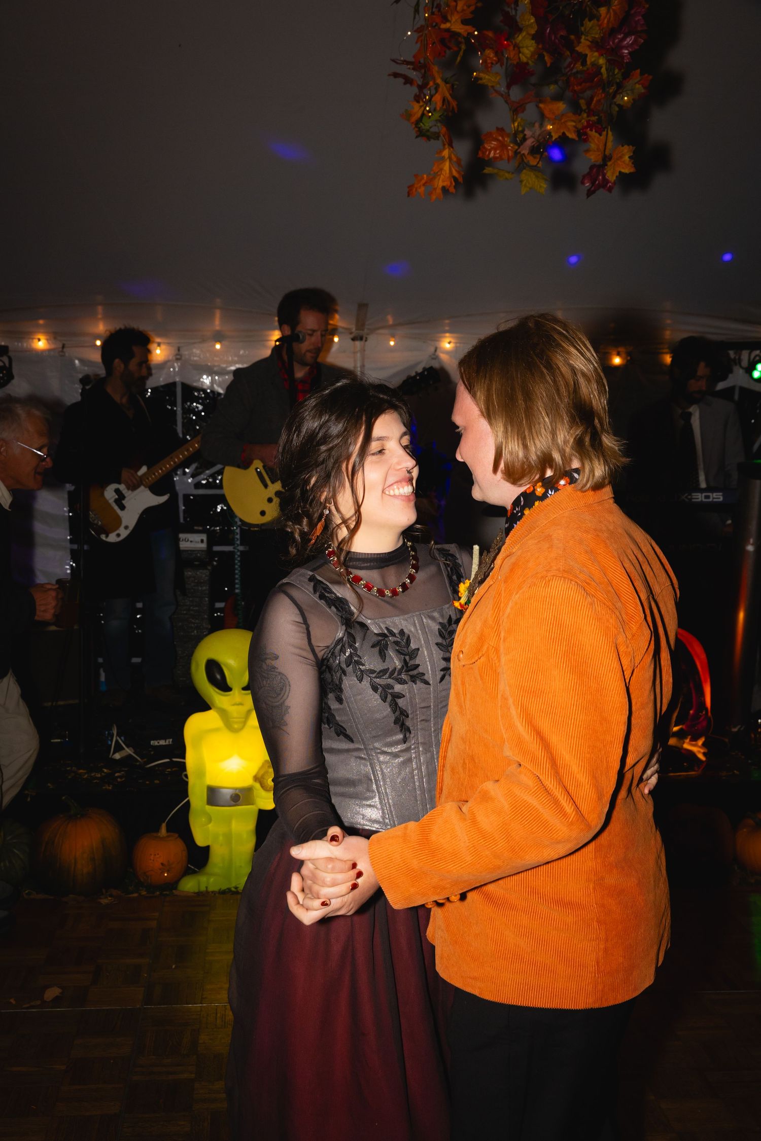 People dancing together in a dimly lit room with orange and purple ambient lighting at an event.