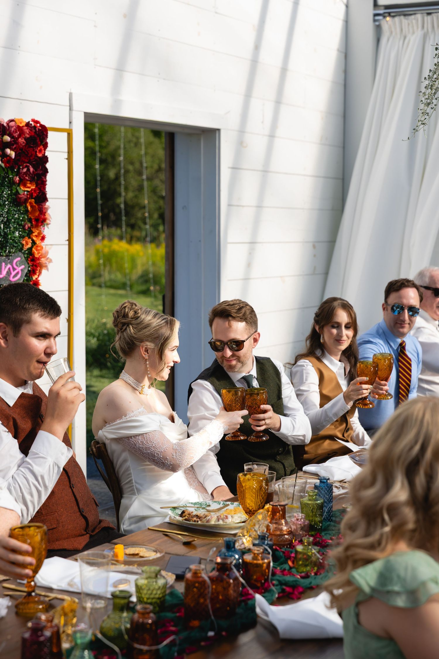 Wedding party guests seated at long tables with amber glassware and floral decorations during a reception.