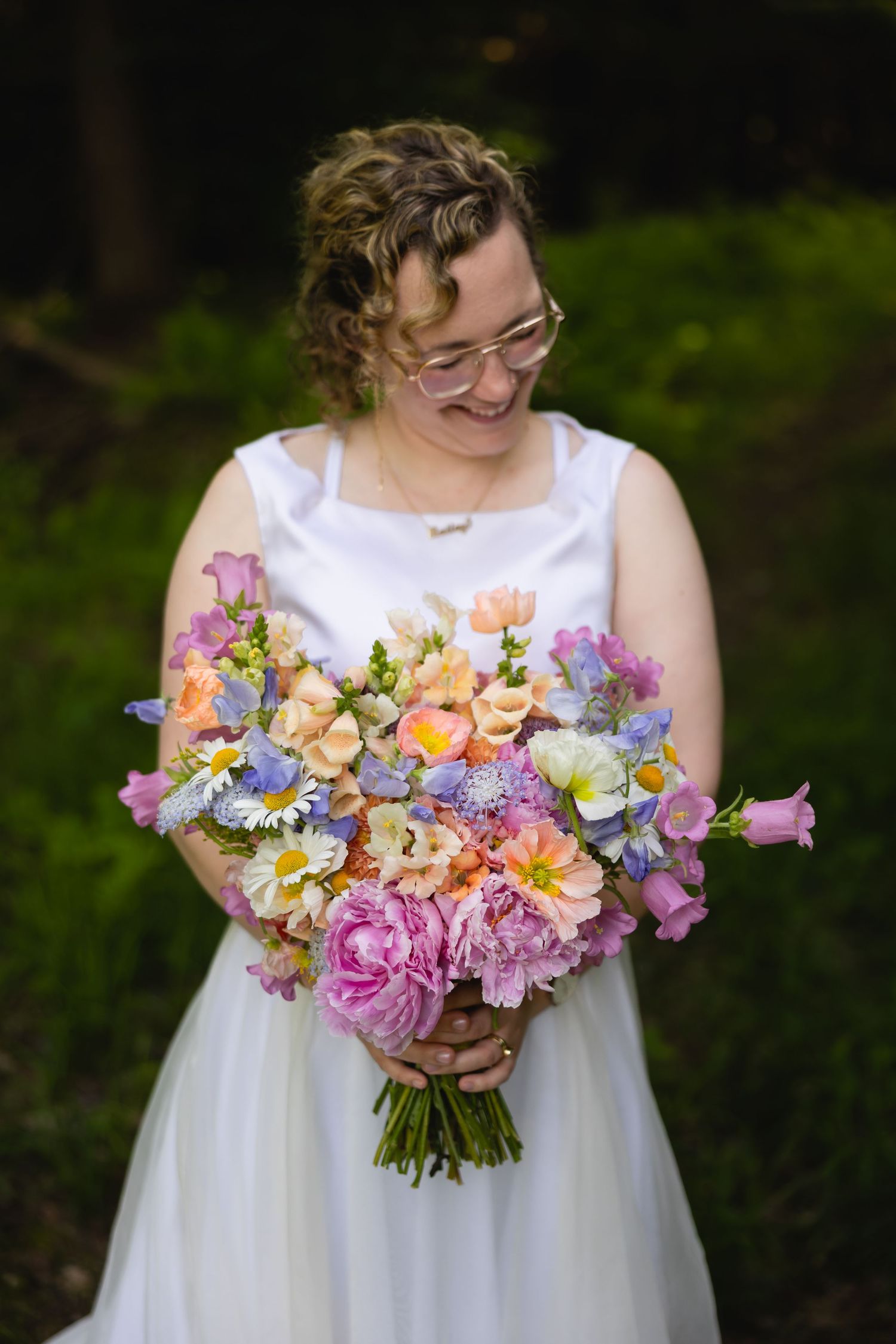 A pastel spring wedding bouquet featuring pink, purple, orange and yellow flowers held against a white dress.