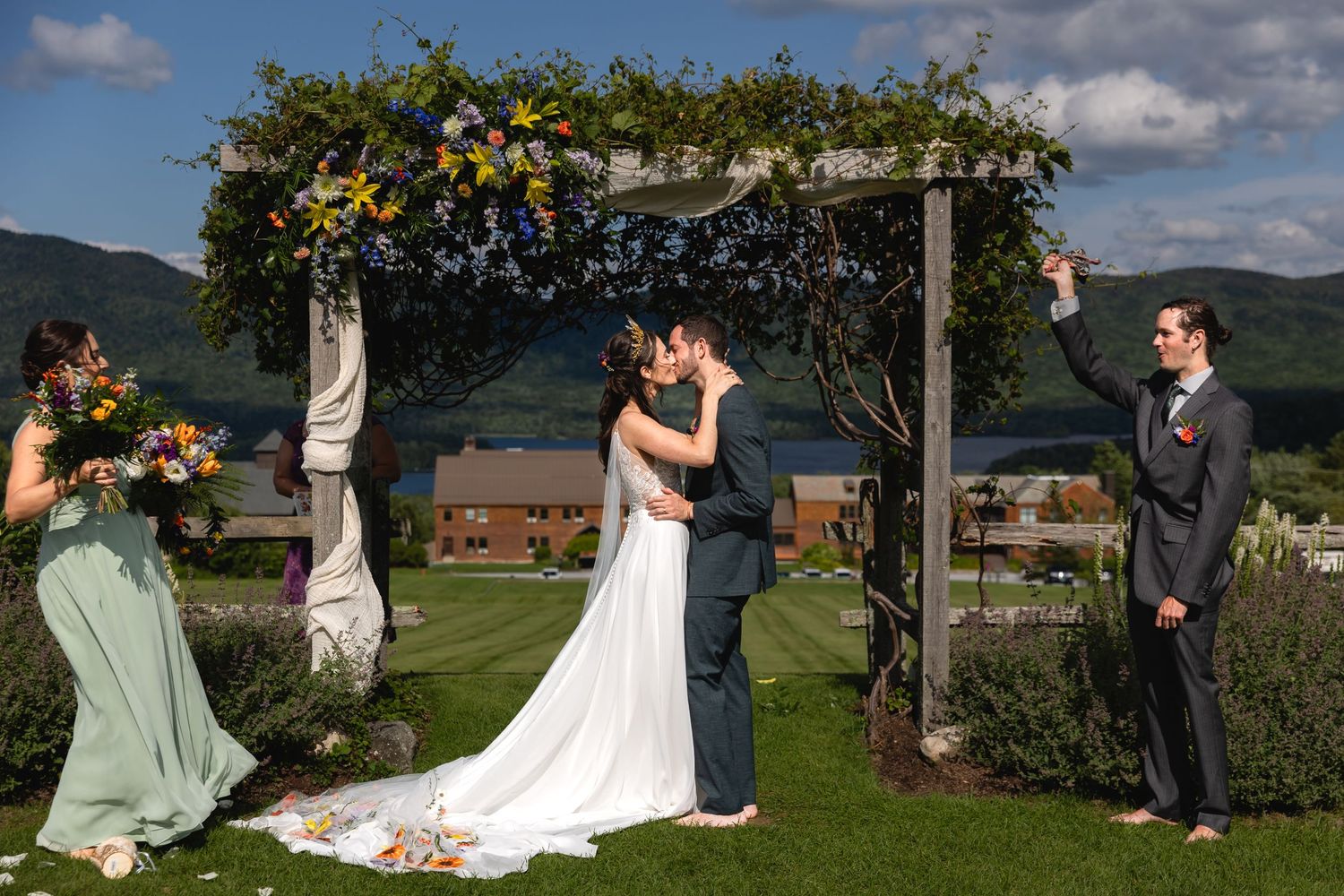 Wedding ceremony under a flower-decorated wooden arch with mountain backdrop.