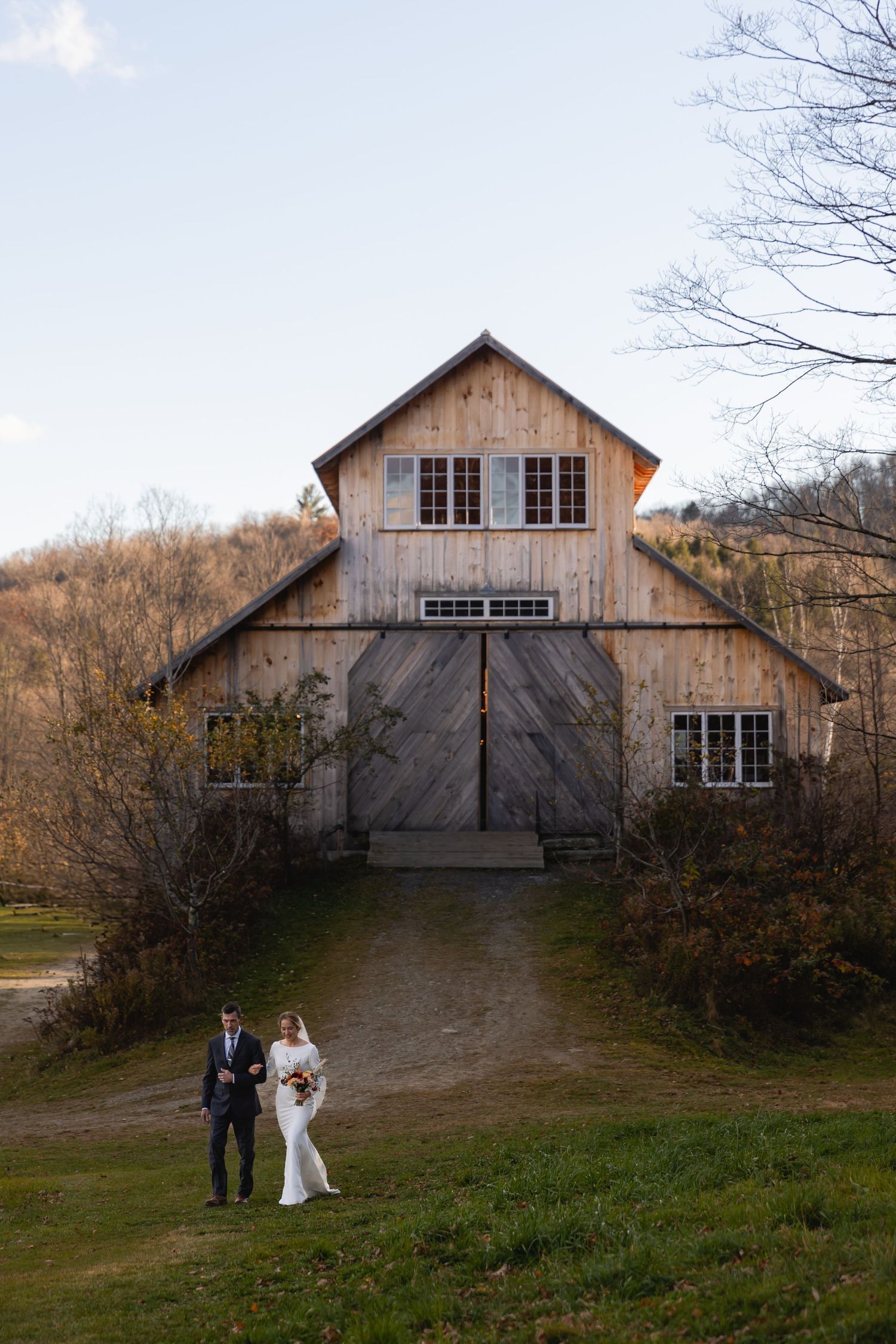 A rustic wooden barn with weathered siding stands on a grassy hill during a rural winter landscape.
