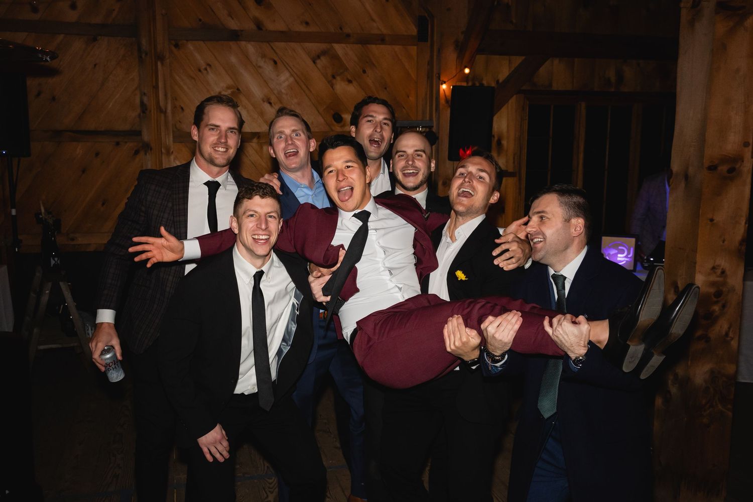 A lively group in formal attire having fun and posing playfully inside a rustic wooden barn.