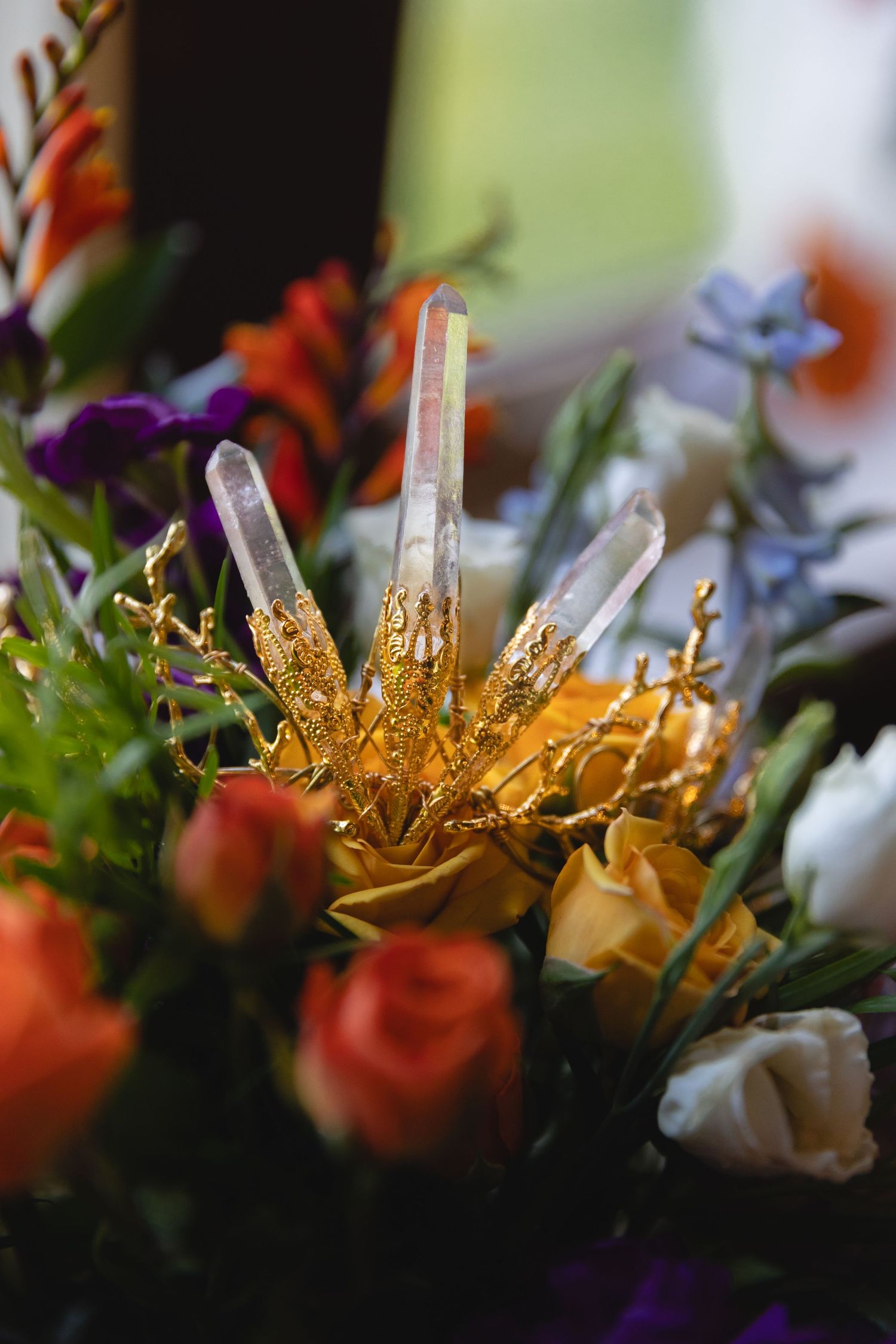 Crystal crown with gold accents surrounded by colorful flowers in a floral arrangement.