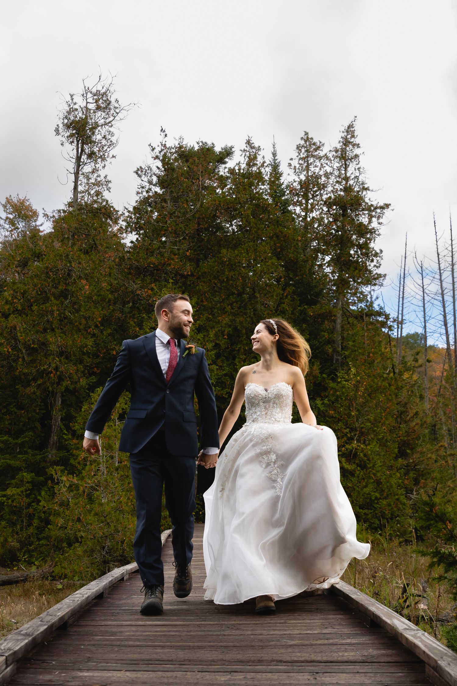 A couple walks together on a wooden boardwalk surrounded by autumn trees.
