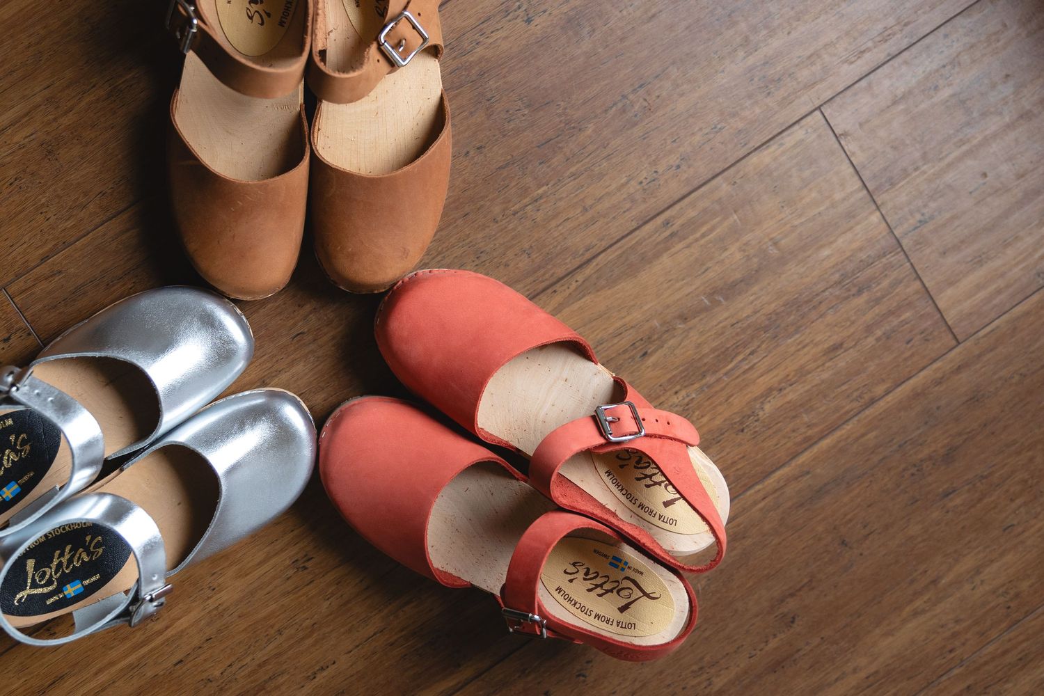 Collection of silver and coral colored shoes arranged on wooden floor.
