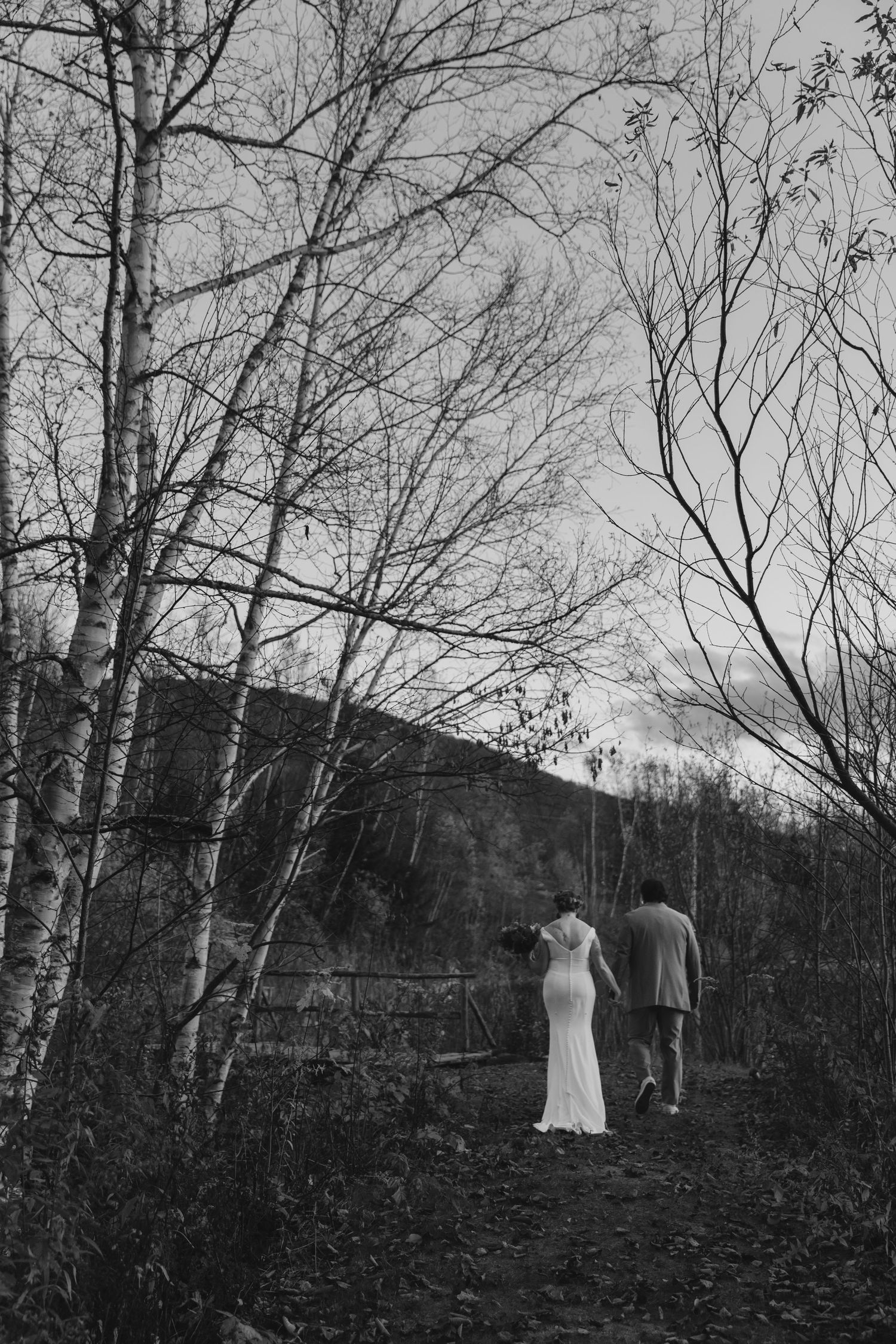 A black and white photo shows a couple walking through bare trees on a hillside path.