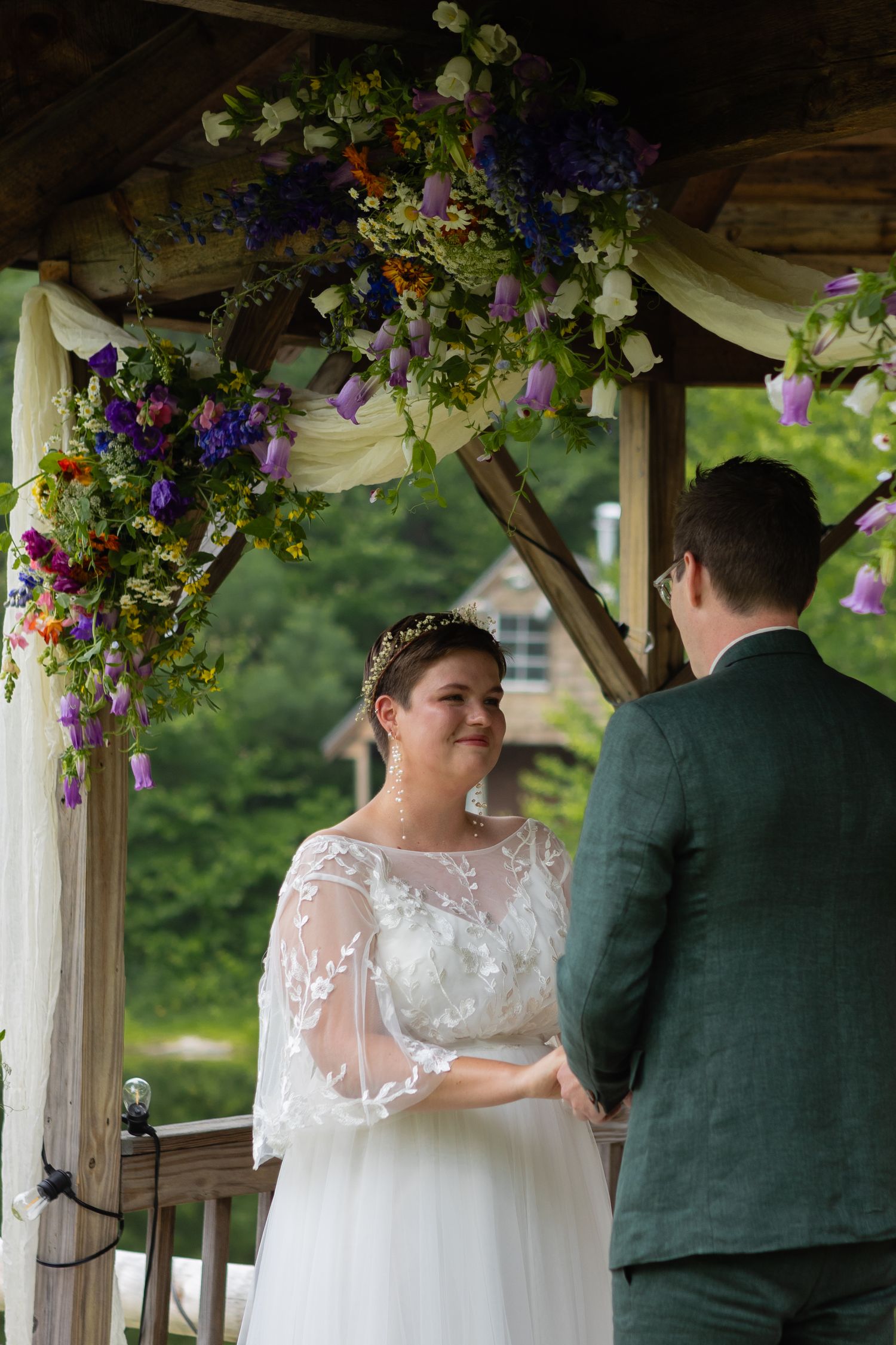 Couple exchanging vows beneath an elegantly decorated gazebo with purple and yellow floral arrangements.