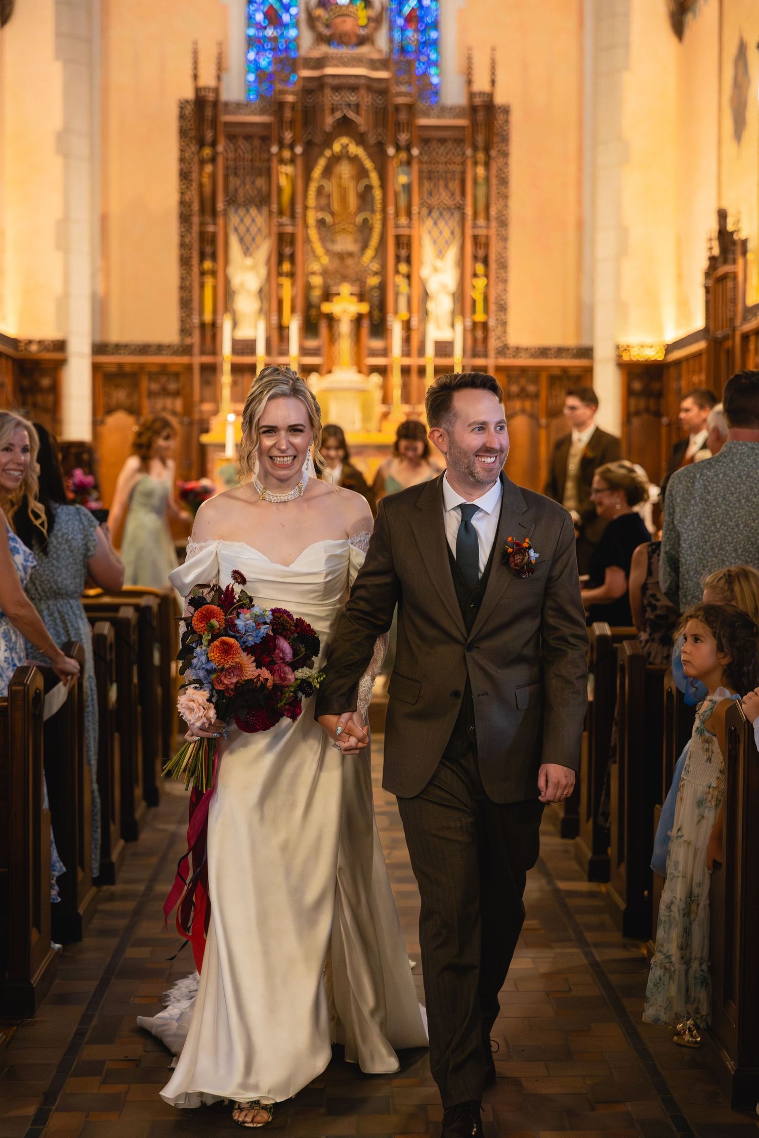 Wedding ceremony processional in a grand church with ornate altars and warm lighting.