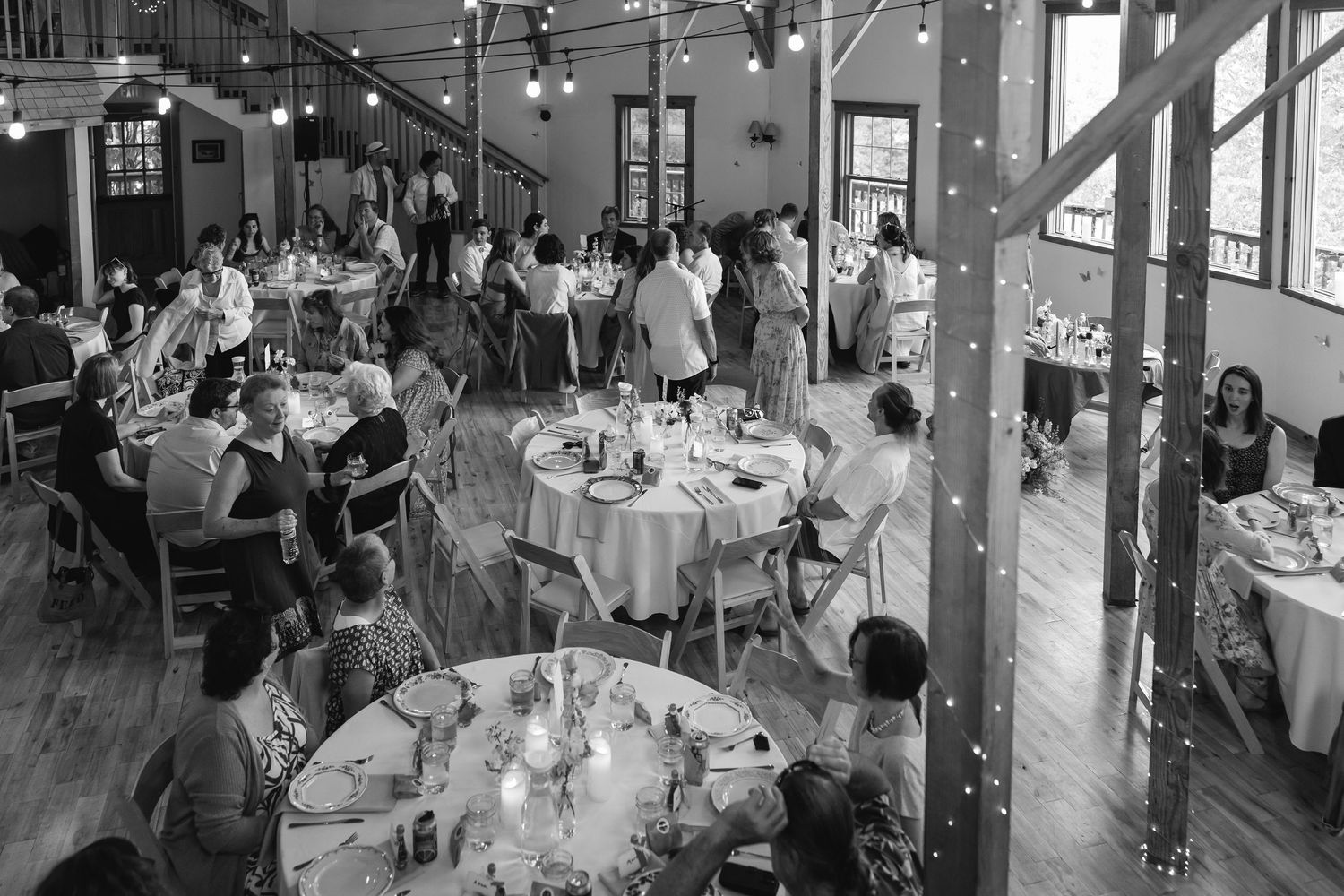 Guests enjoy a wedding reception in an industrial-style venue with exposed beams and large windows.