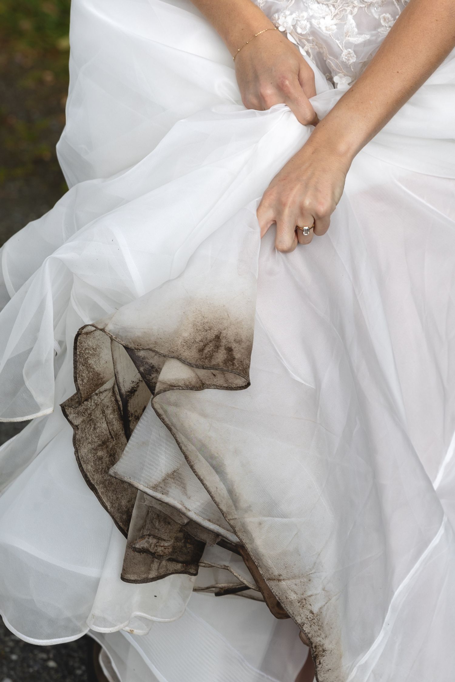 Close-up of a bride holding her muddy white wedding gown hem, showing dirt stains on the dress.