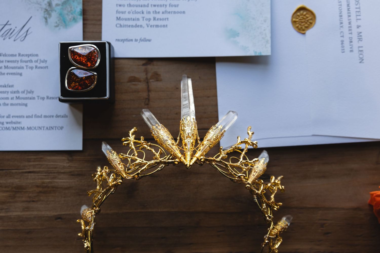 Golden crown and wedding stationery details arranged on wooden surface.