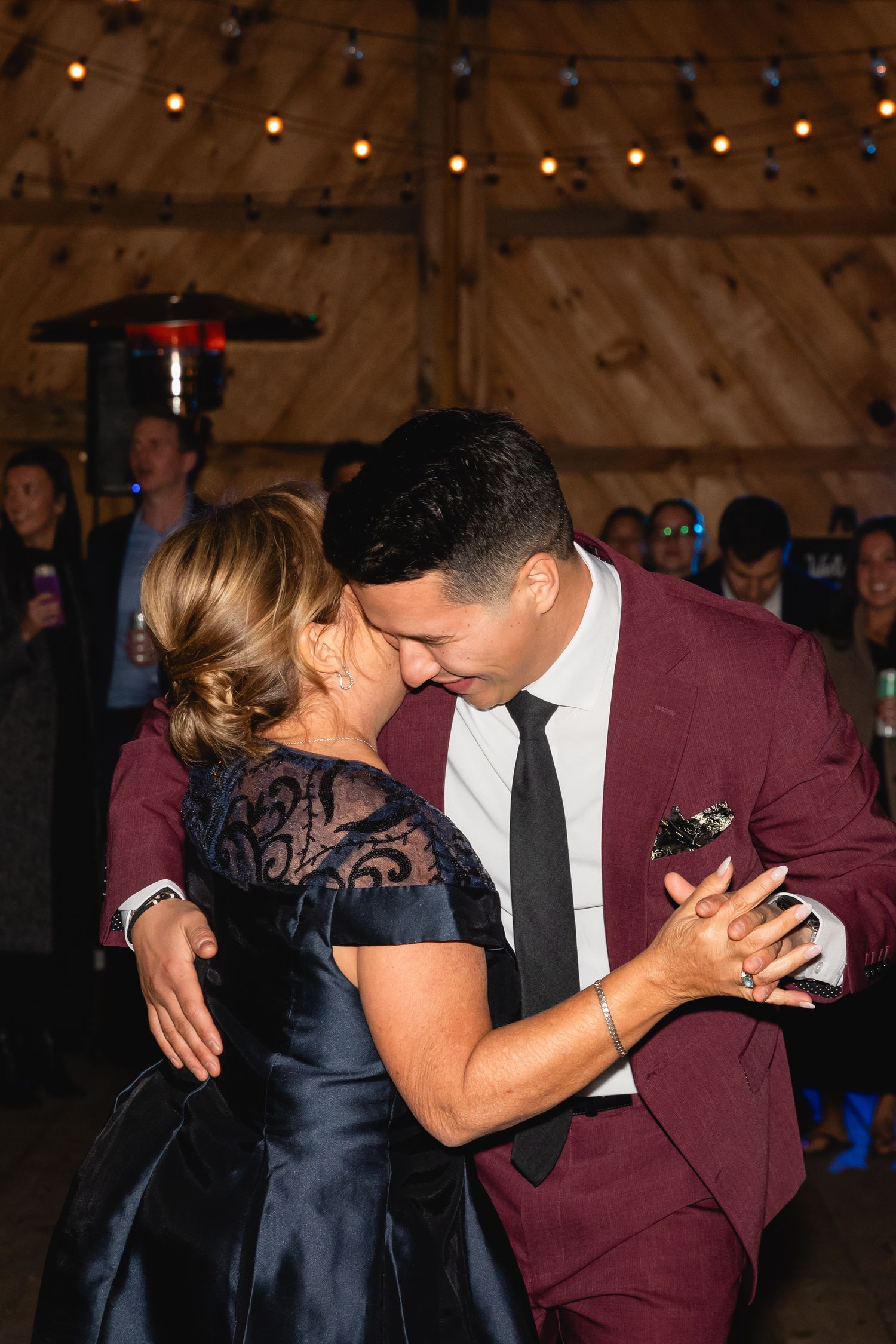 A tender dance under warm lights in a rustic barn setting with string lights overhead.