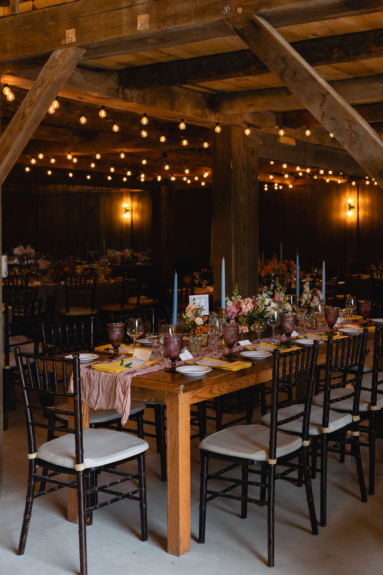 Rustic barn reception venue with wooden farm tables, chiavari chairs and string lights creating warm ambiance.